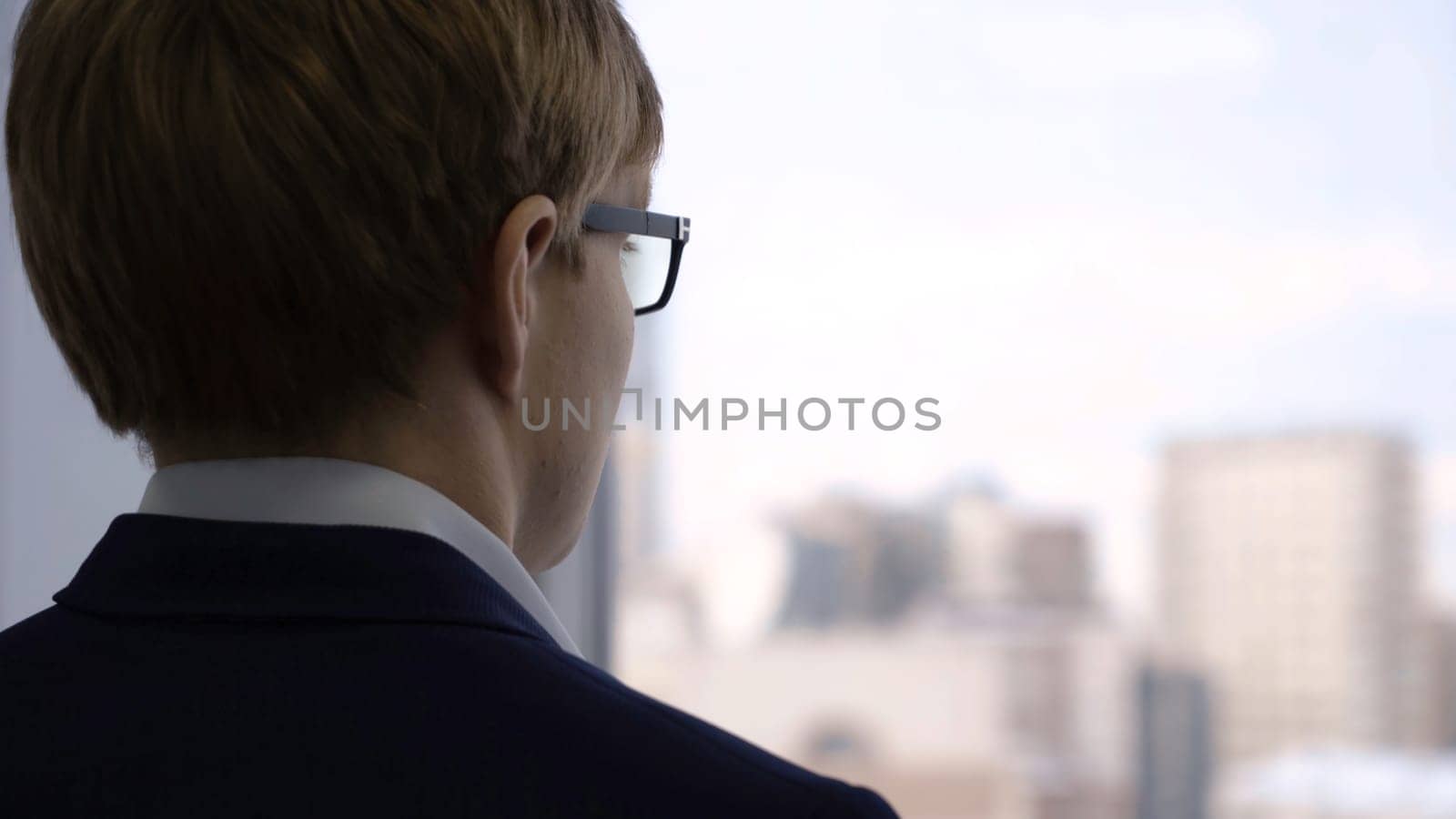 Close-up businessman looking out window. Young manager with thoughtful expression looks out window through glasses and thinks about work.