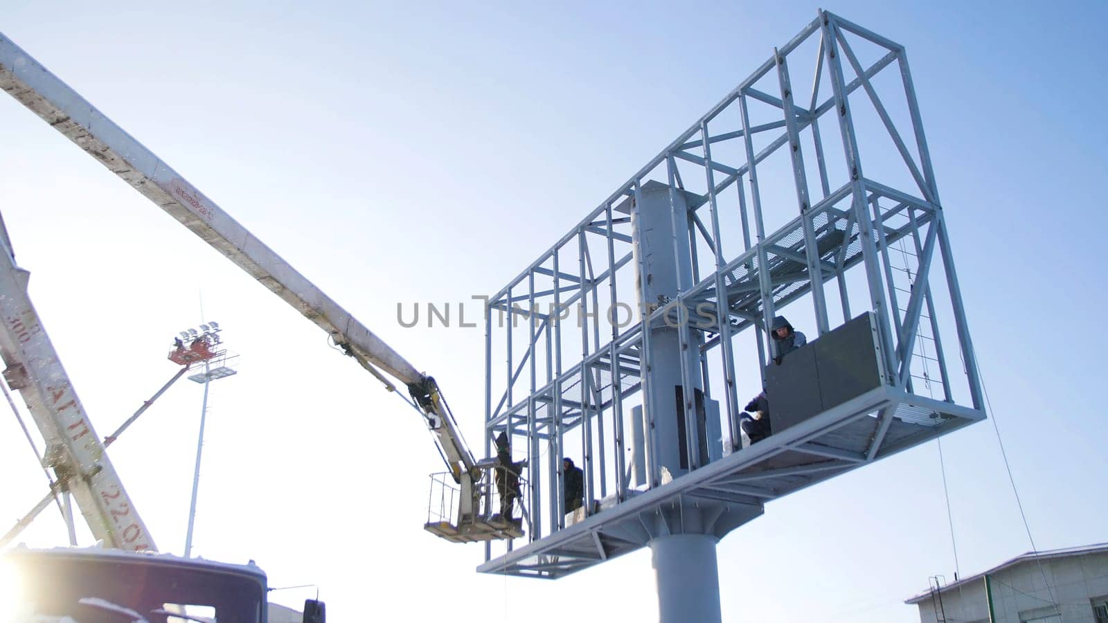 Builder on a Lift Platform at a construction site. Men at work. construction worker assembling scaffold on building site. Men assemble Billboard on tap.