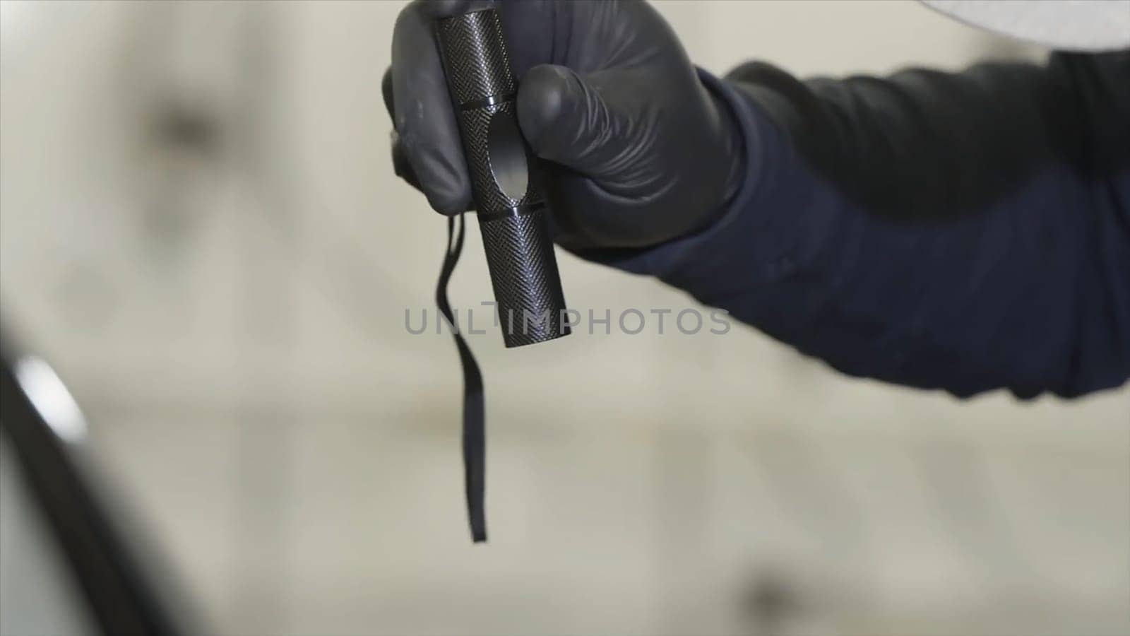 Close up for male hand in black glove holding black flashlight with narrow beam at the repair shop. Man holding small flashlight during working process.