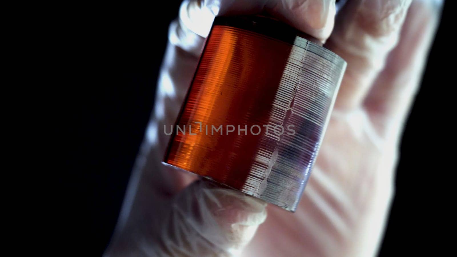 Burned piece of orange mineral. Close-up of gloved hands holding piece of processed amber mineral on black background.