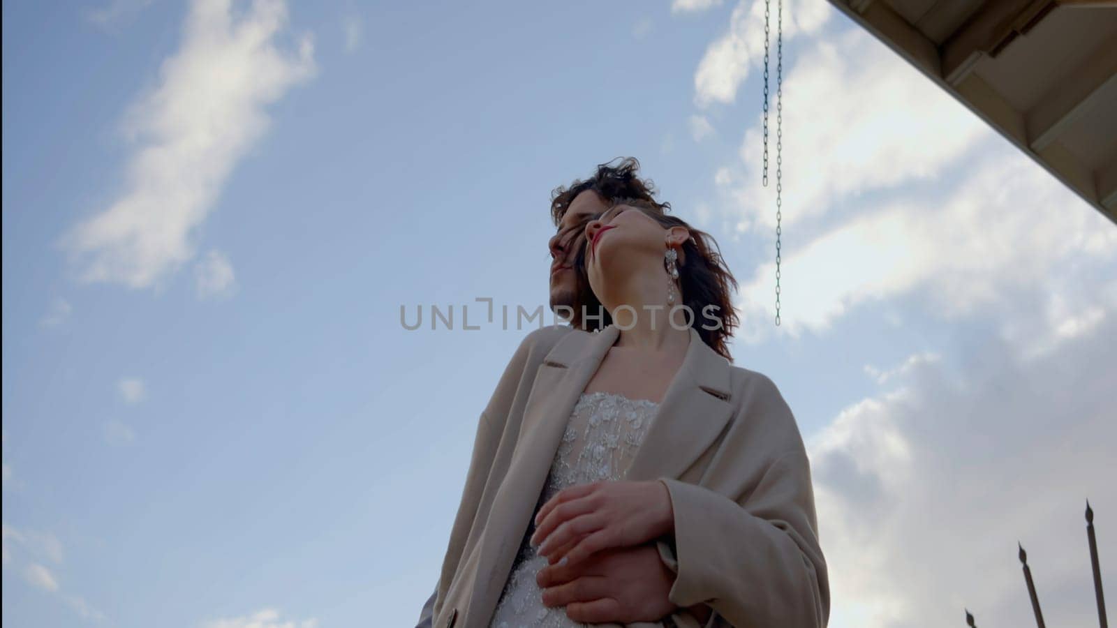 A couple embracing through the eyes of a photographer. Action.Newlyweds standing next to the bridge in nature with the wind blowing and gently hugging each other. High quality 4k footage