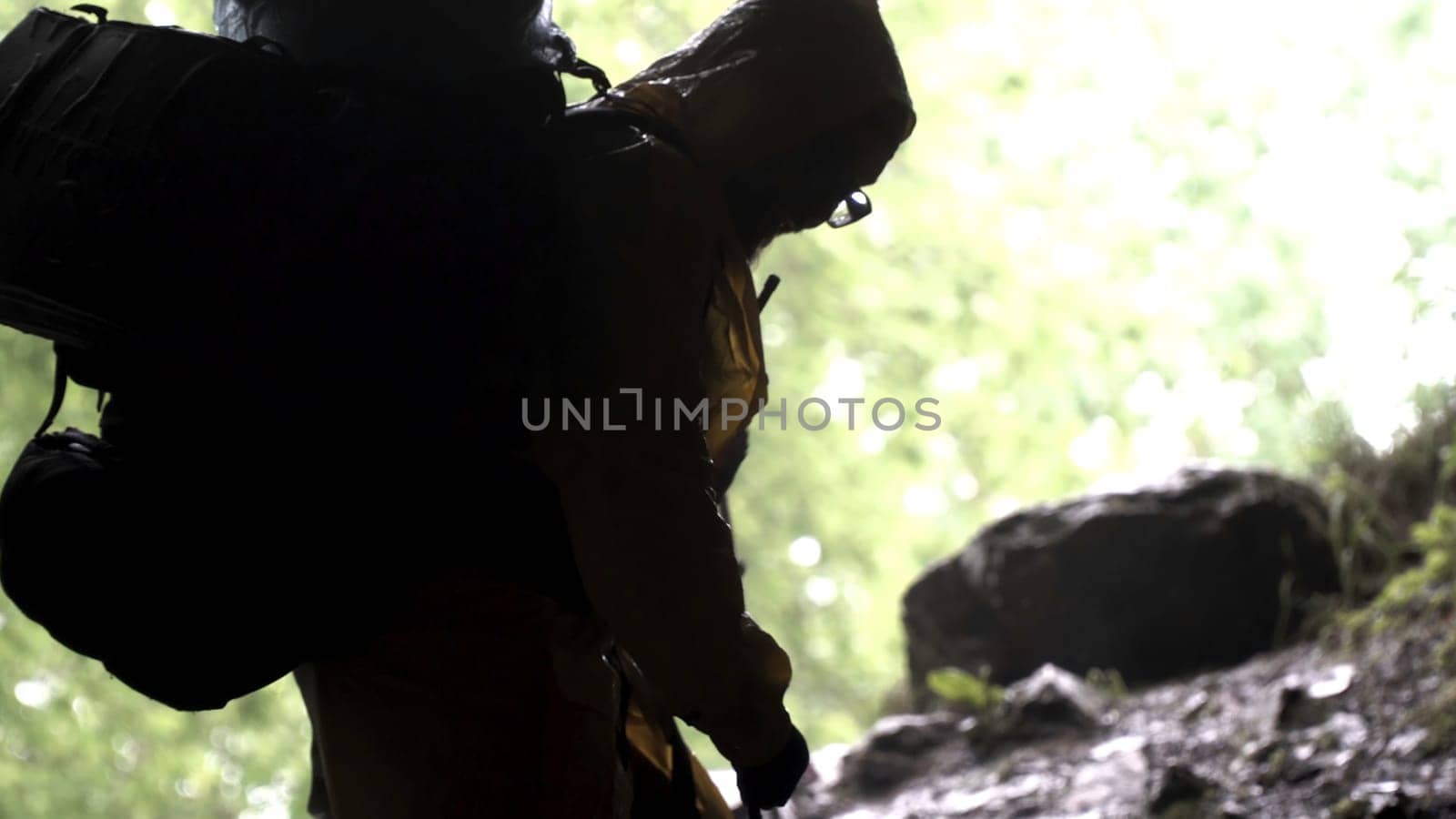 Young explorer standing in a cave with climbing equipment ready for action, travelling and extreme concept. View from the inside of the cave with climbing person.