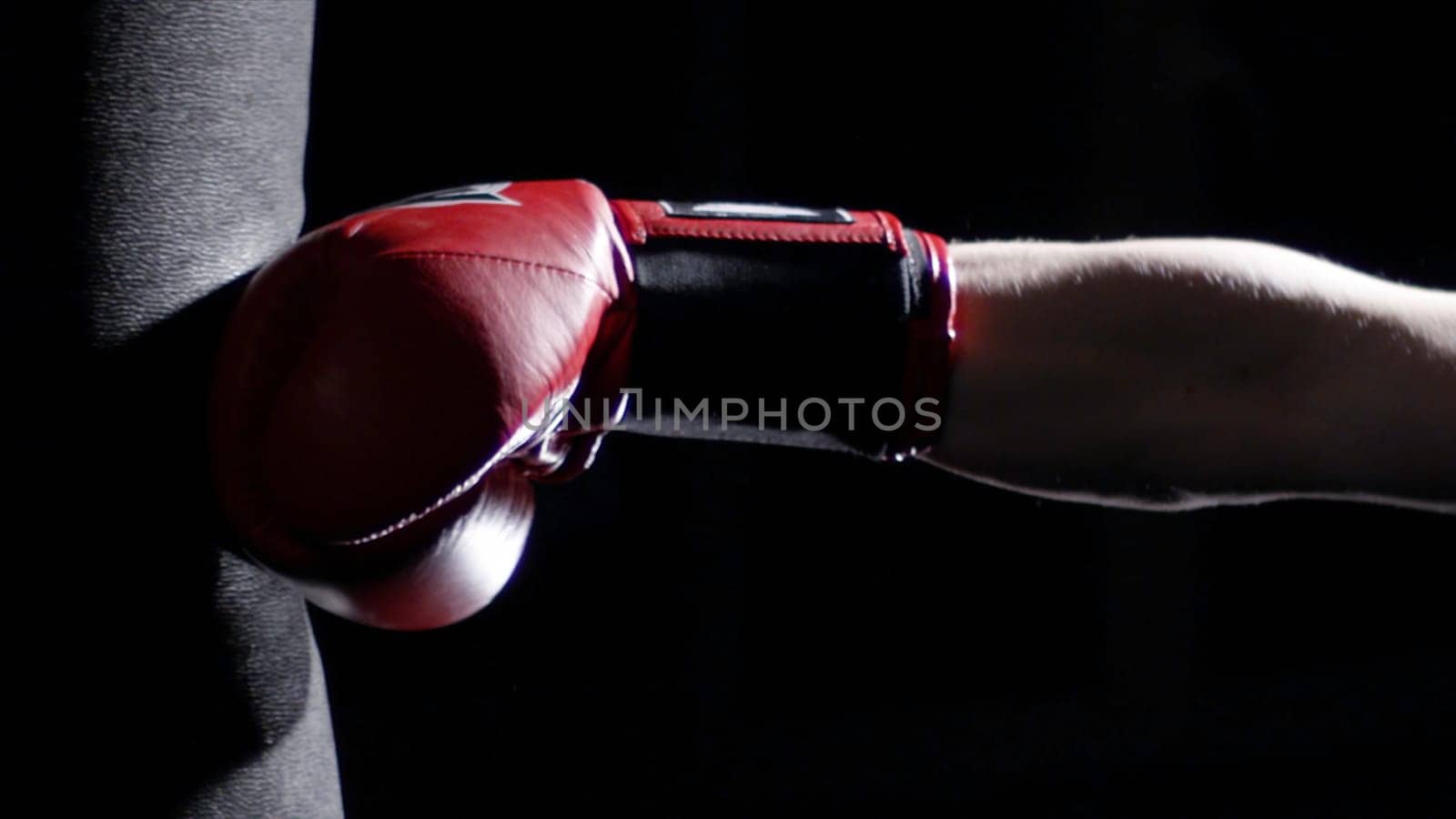 Fighter Practicing Some Kicks With Punching Bag - A Man With A Tattoo Boxing On dark Background. Kick, punching bag on dark background. Black punching bag weighs at the gym.