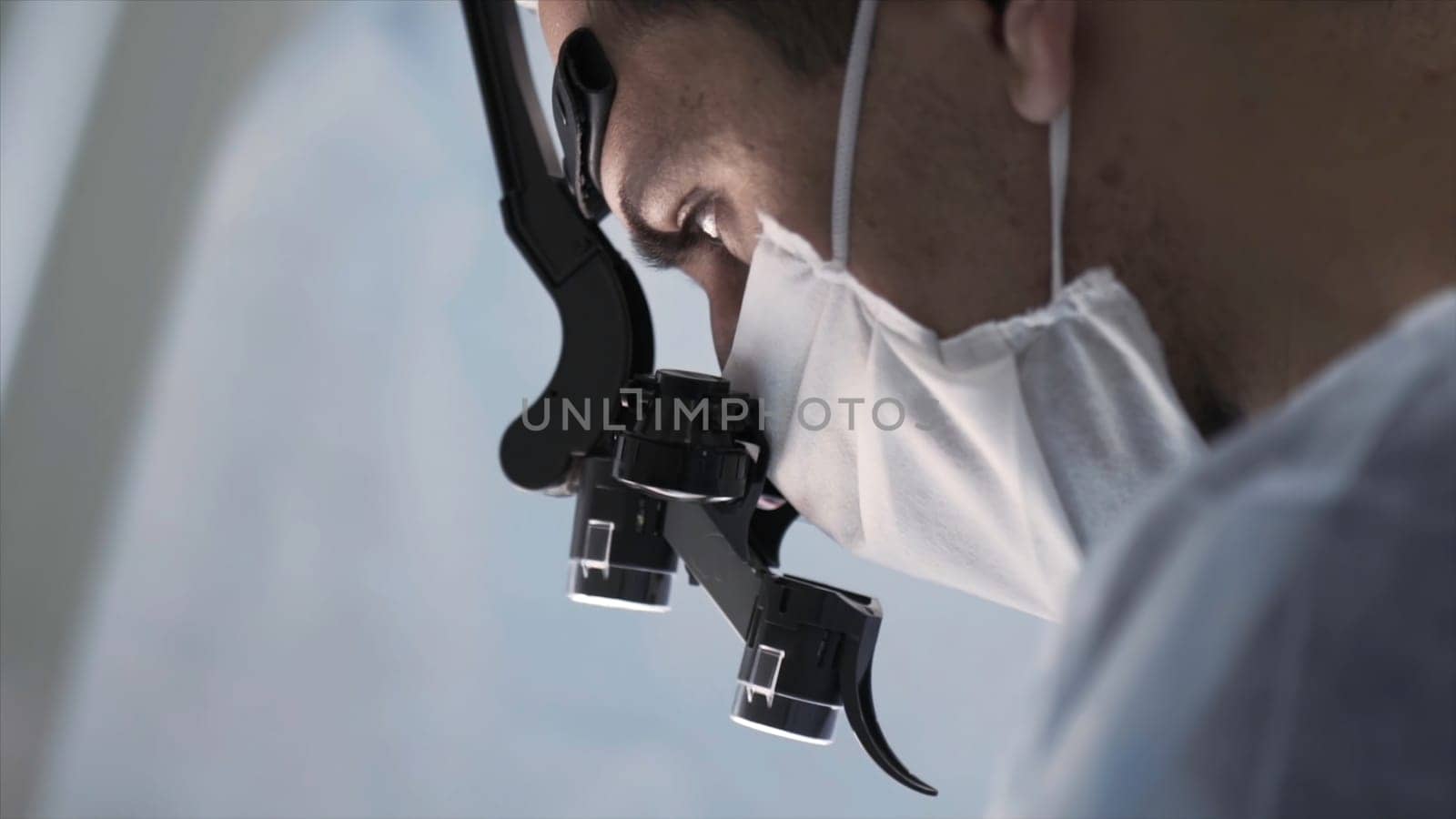 Surgeon head with professional glasses at work. Close up side view of a doctor in glasses with binocular magnifiers examines something at laboratory.