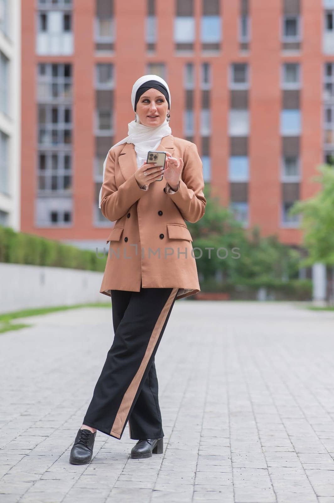 Young woman in hijab using smartphone outdoors