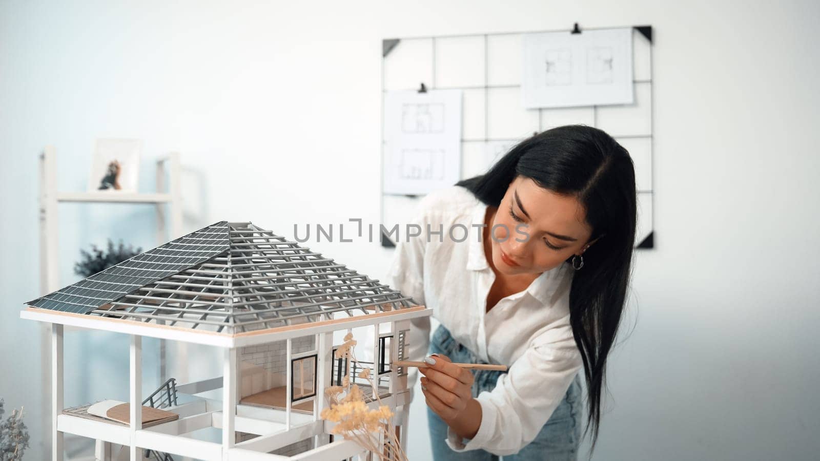 Young beautiful caucasian architect engineer turns house model around to inspect house construction and check mistake point to solve the problem on meeting table at modern office. Closeup. Immaculate.