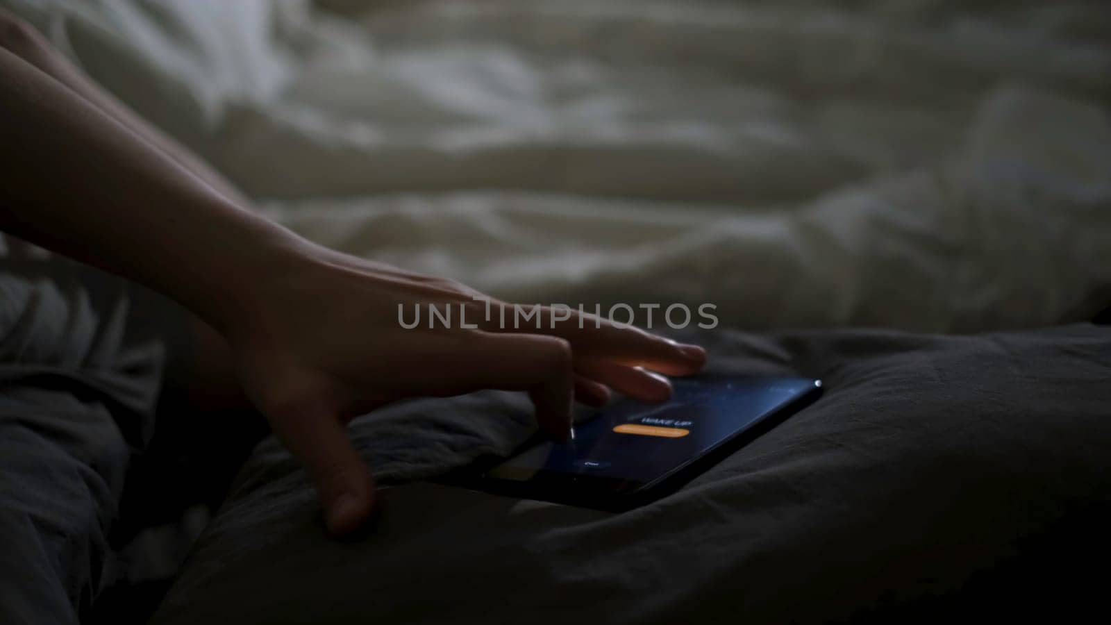 Close up of sleeping man being woken up by his phone lying on the bed. Male hand trying to turn off the alarm clock lying near on a blanket at home early in the morning.