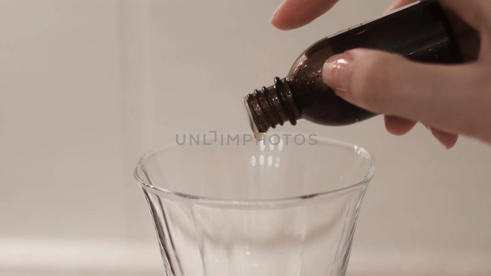 Close-up of medicine dripping from bottle into clear glass. Concept. Woman drops medicine into glass on white isolated background. Treatment or poison.