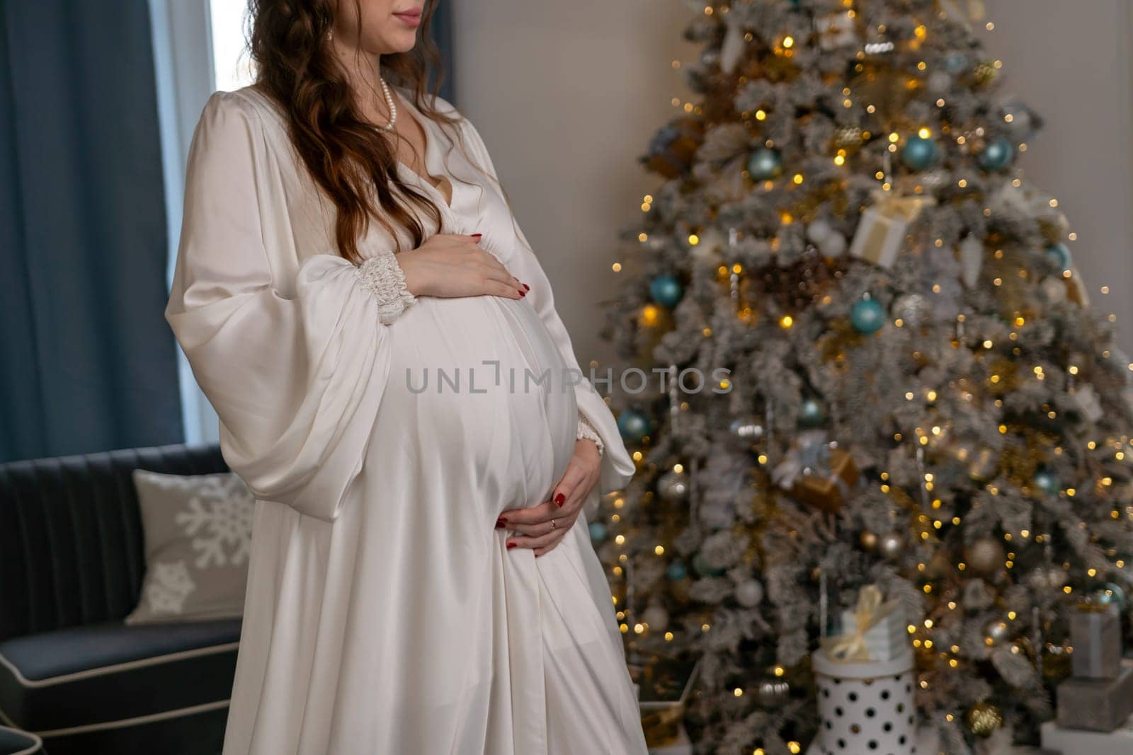 Pregnant woman holding a belly against Christmas tree with lights. family holiday concept