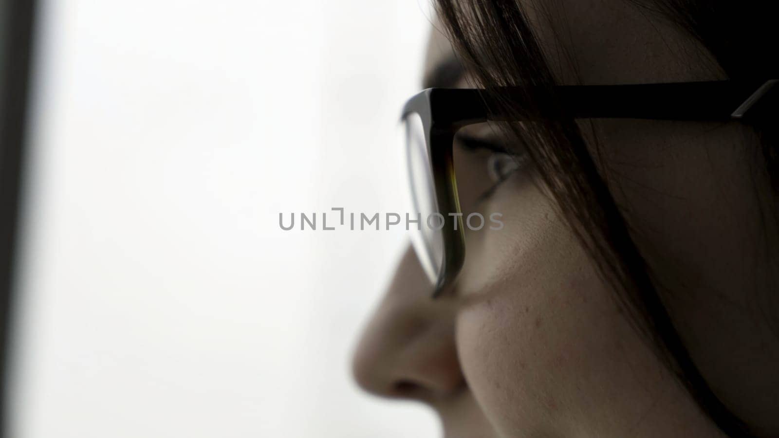 Extreme close up for young female face portrait in profile in black glasses on fuzzy, white background. Beautiful woman with her face in profile and short, dark hair