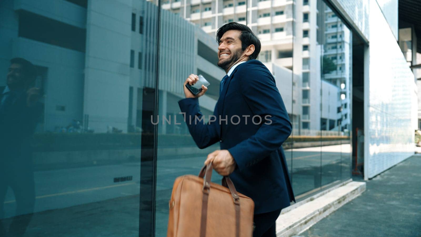 Skilled smart business man dancing with joyful while walking in glass wall. Project manger receive a good news, getting promotion, getting a successful job while express feeling of overjoy. Exultant.