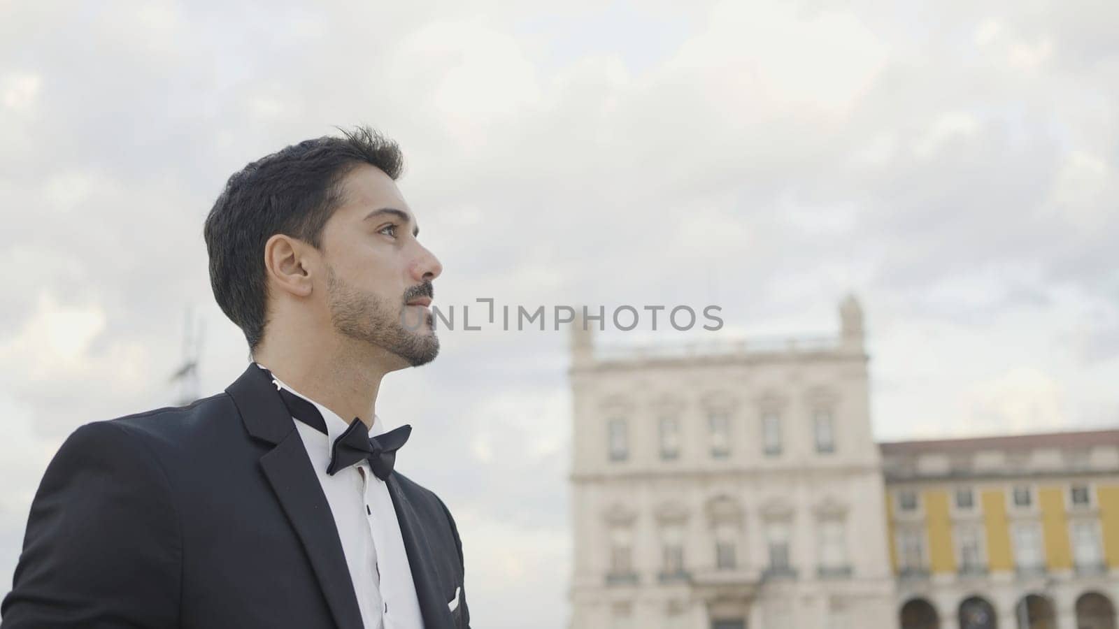 Handsome man in suit walks down street on summer day. Action. Attractive man in suit goes on date or event. Elegant man in suit walks confidently down street.