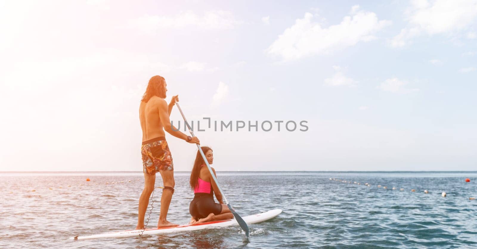 Sea woman and man on sup. Silhouette of happy young woman and man, surfing on SUP board, confident paddling through water surface. Idyllic sunset. Active lifestyle at sea or river