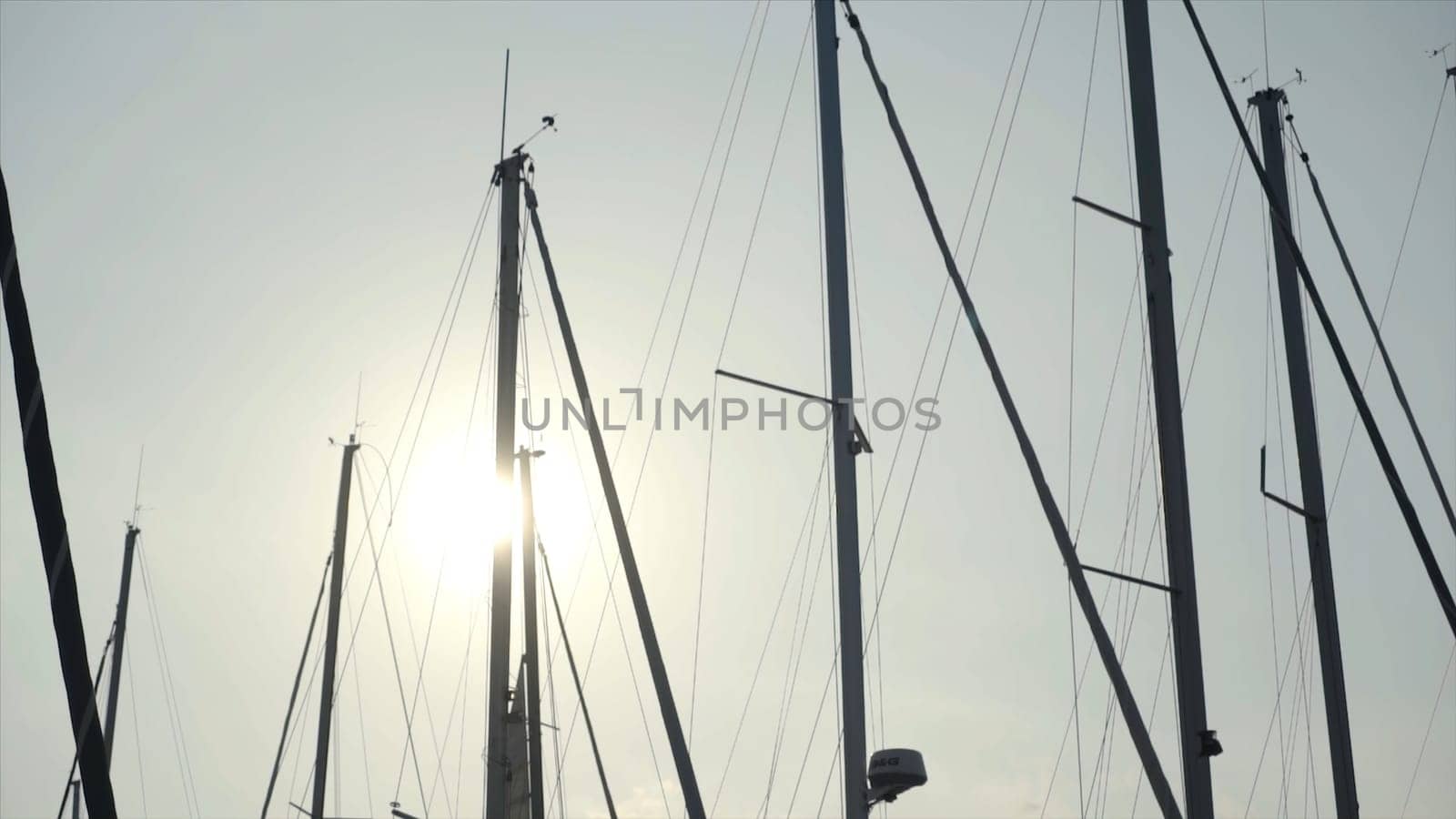 Beautiful view of masts of ships on background of sun and blue sky. Action. Masts of yachts are illuminated by warm sunlight beckoning to sea journey.