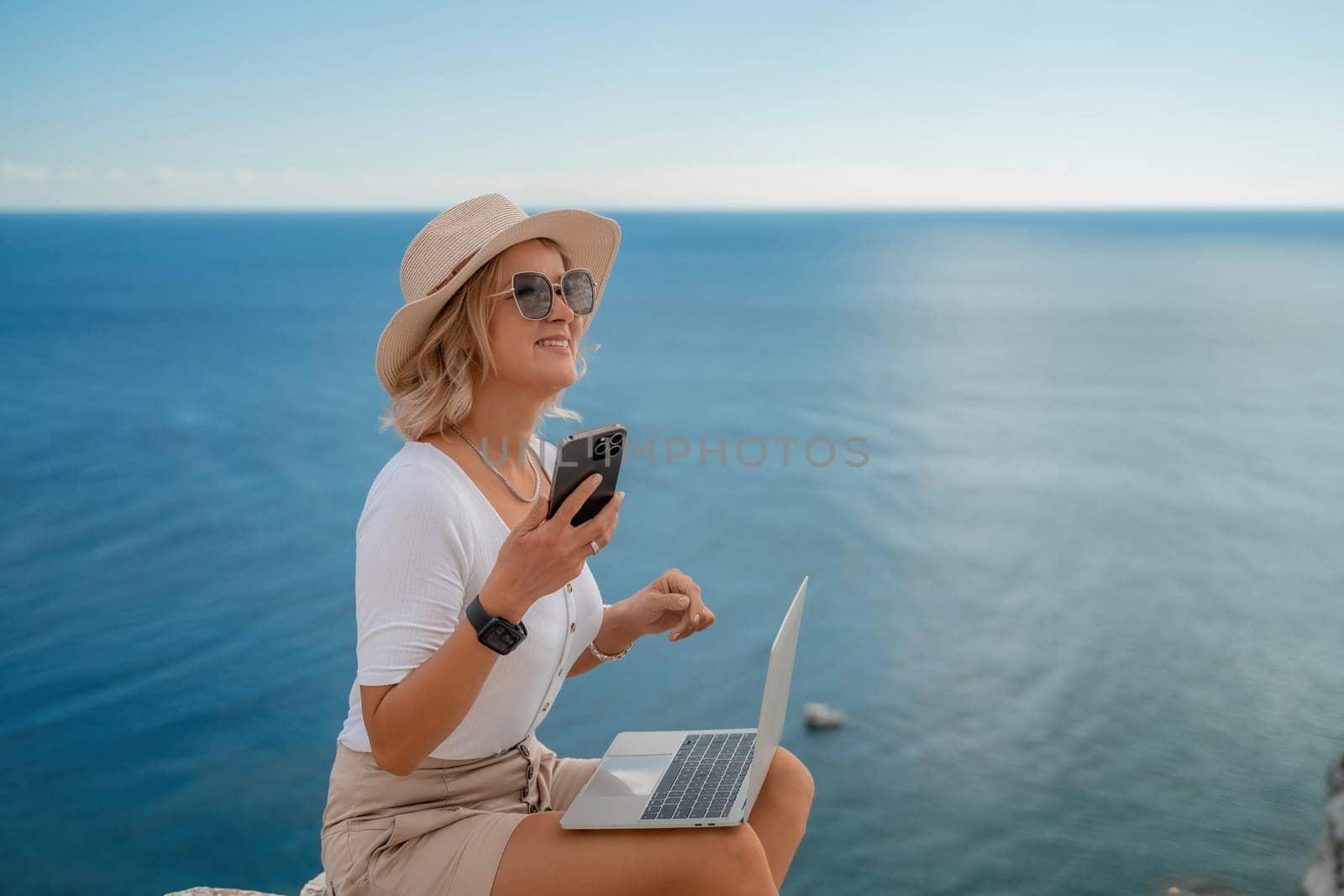 Freelance women sea working on the computer. Good looking middle aged woman typing on a laptop keyboard outdoors with a beautiful sea view. The concept of remote work