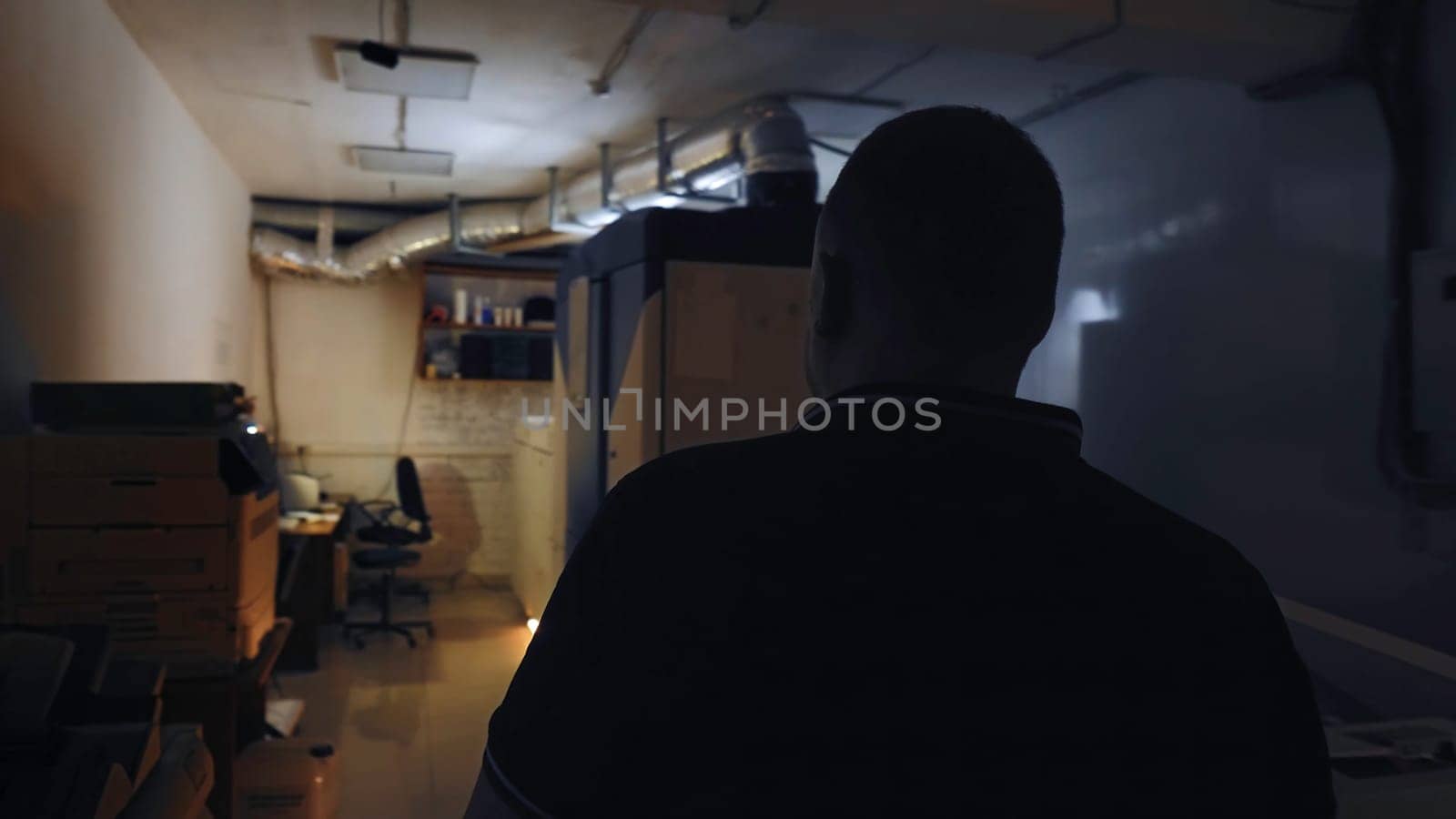 Workplace in office cubicle. Stock footage. Man walks across dark, small room to light-colored Desk in corner. Office worker works in copy room with document warehouse.