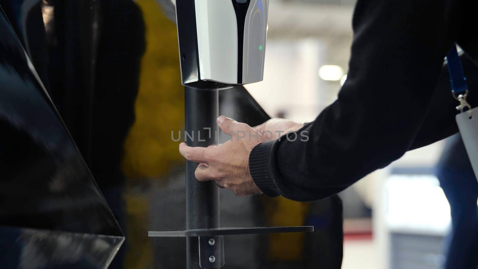 Close-up of hand dispenser at entrance. Media. Automatic dispenser with sensor for spraying antibacterial agent on hands. Man passes through dispenser with antibacterial agent.