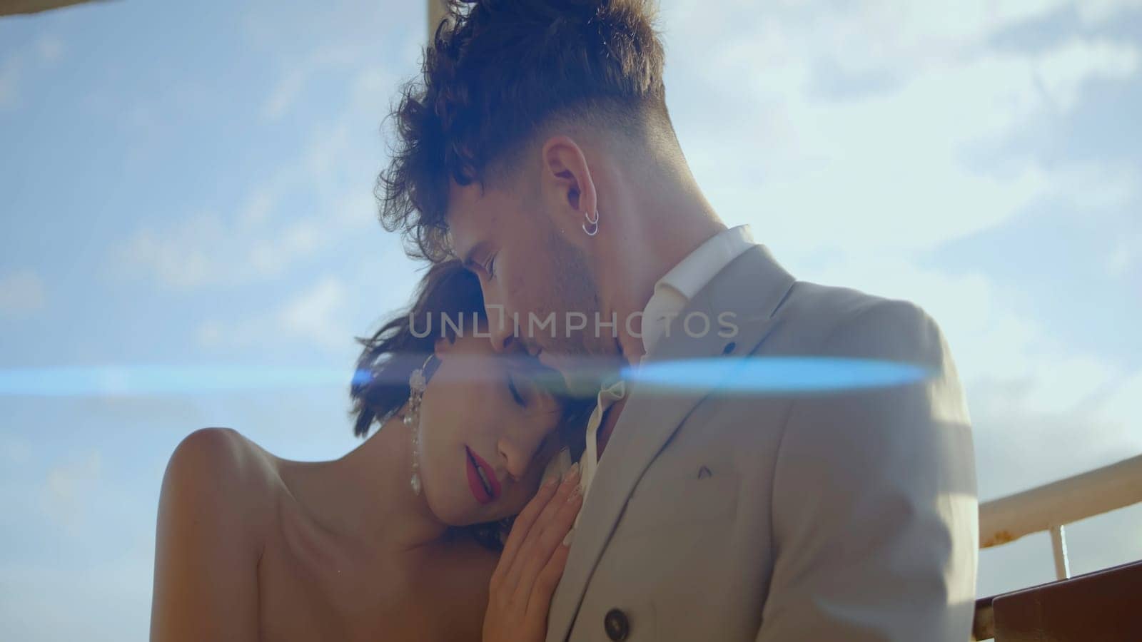 Beautiful newlyweds hug on background of blue sky. Action. Stylish couple embracing in love on sunny day. Newlyweds hug on clear windy day by Mediawhalestock