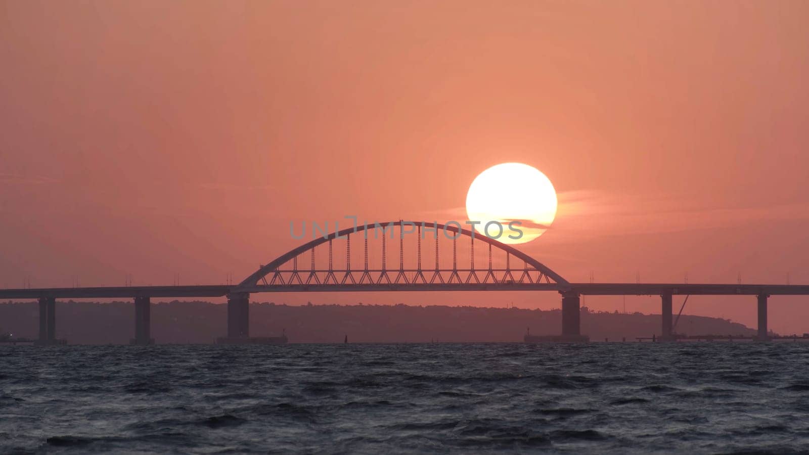 Stunning view of the beautiful sunset over the big river and the bridge, time lapse effect. Bright golden sun moving towards the horizon above the river.