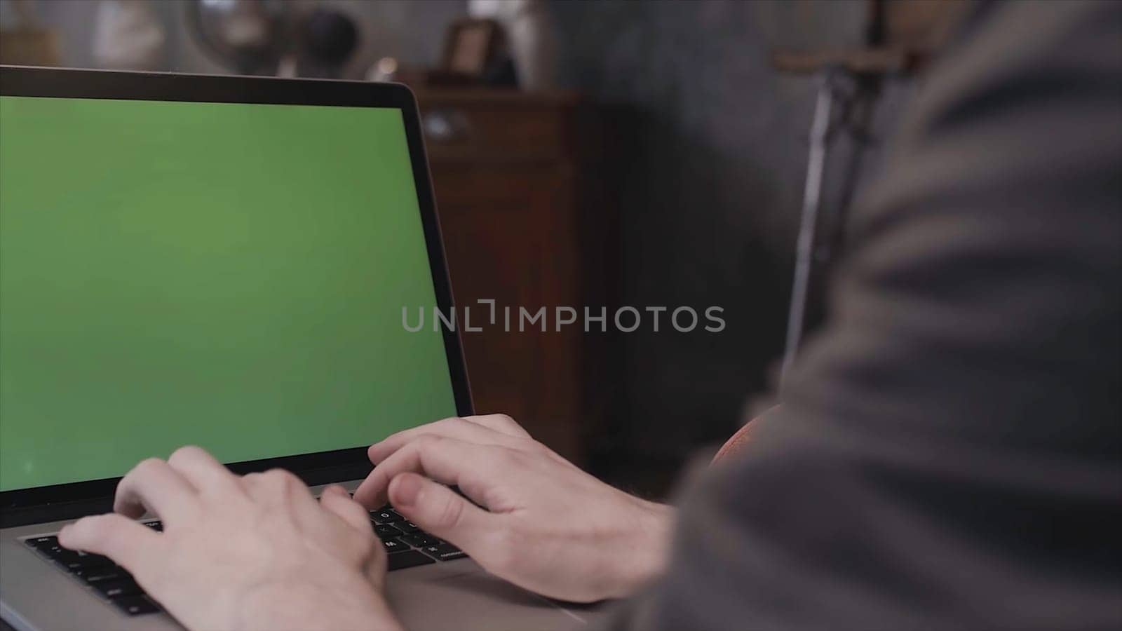 Close up rear view of young businessman hands typing on a laptop keyboard with a blank green editable screen. Man using laptop with chroma key.