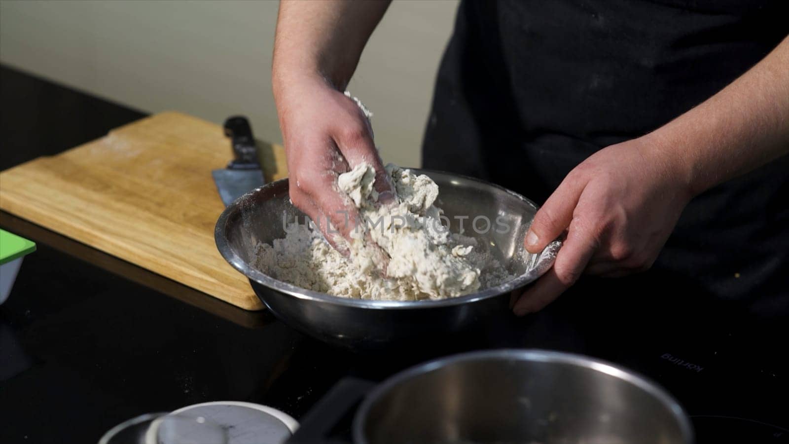 Man kneading dough with his hands in a metal bowl at the kitchen. Art. A cook preparing dough, mixing ingredients with his hands