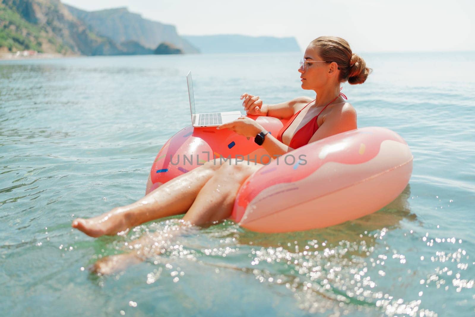 Woman laptop sea. Freelancer woman in sunglases floating on an inflatable big pink donut with a laptop in the sea. People summer vacation rest lifestyle concept by Matiunina