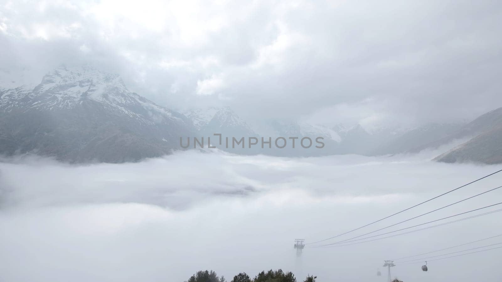 Beautiful mountain landscape with thick clouds. Creative. Rocky snowy mountain peaks with cloudy clouds. Low cumulus clouds in snowy mountains in autumn.