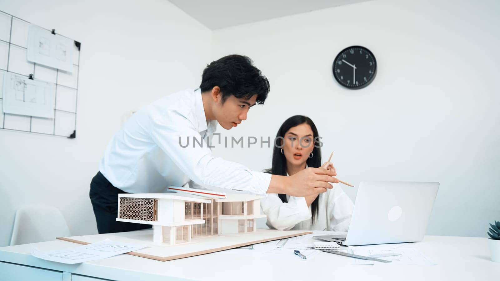 Architect measures house model length while colleague using laptop. Immaculate. by biancoblue