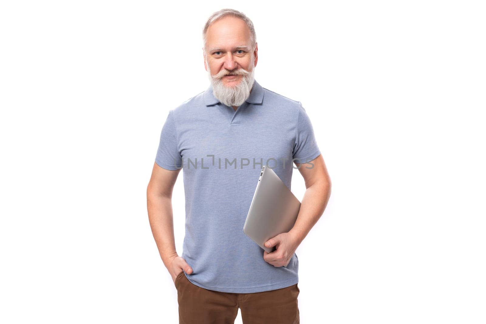 cute smart old man with mustache and beard dressed in a t-shirt works in an IT company using a laptop.