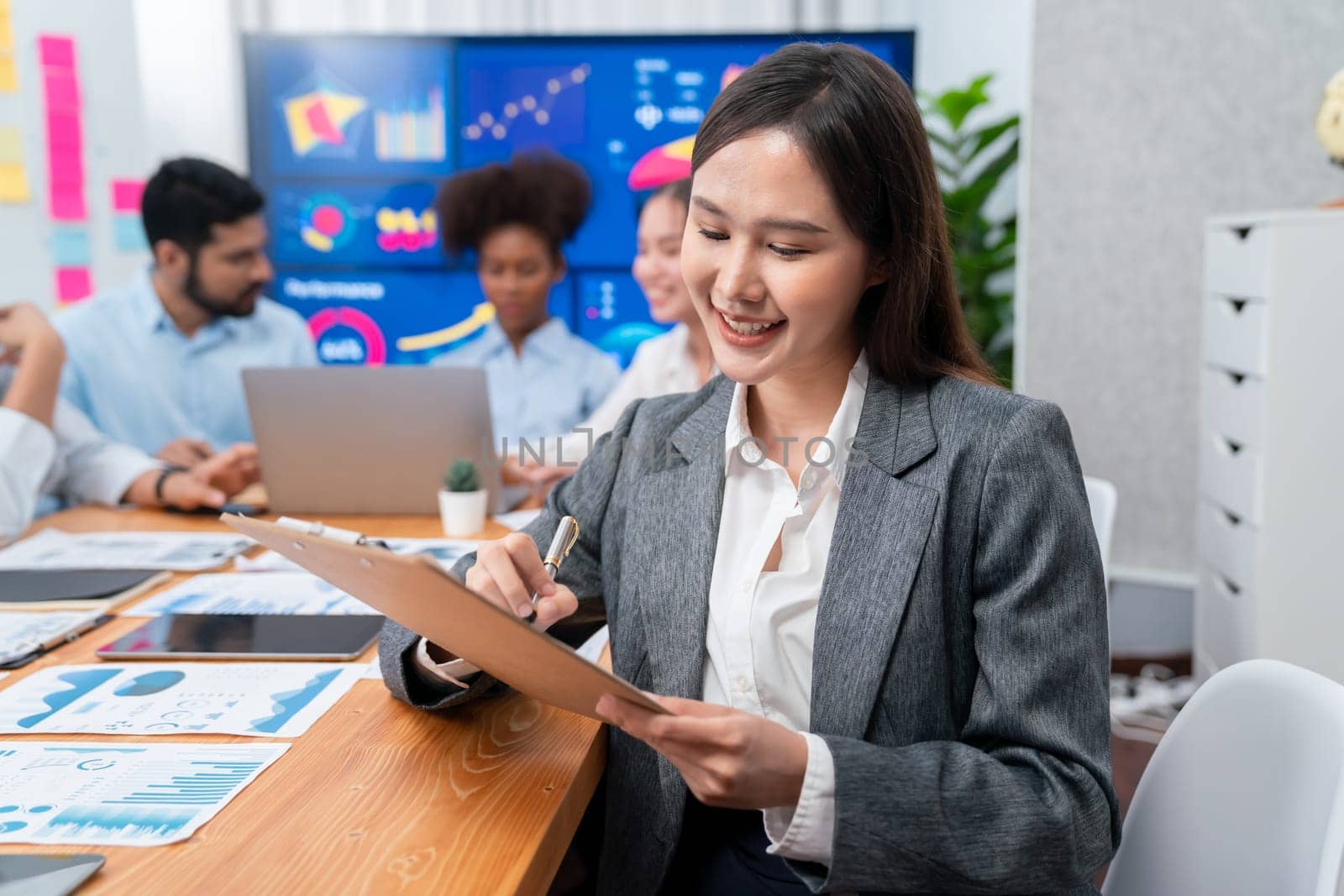 Portrait of happy young asian businesswoman with group of office worker on meeting with screen display business dashboard in background. Confident office lady at team meeting. Concord