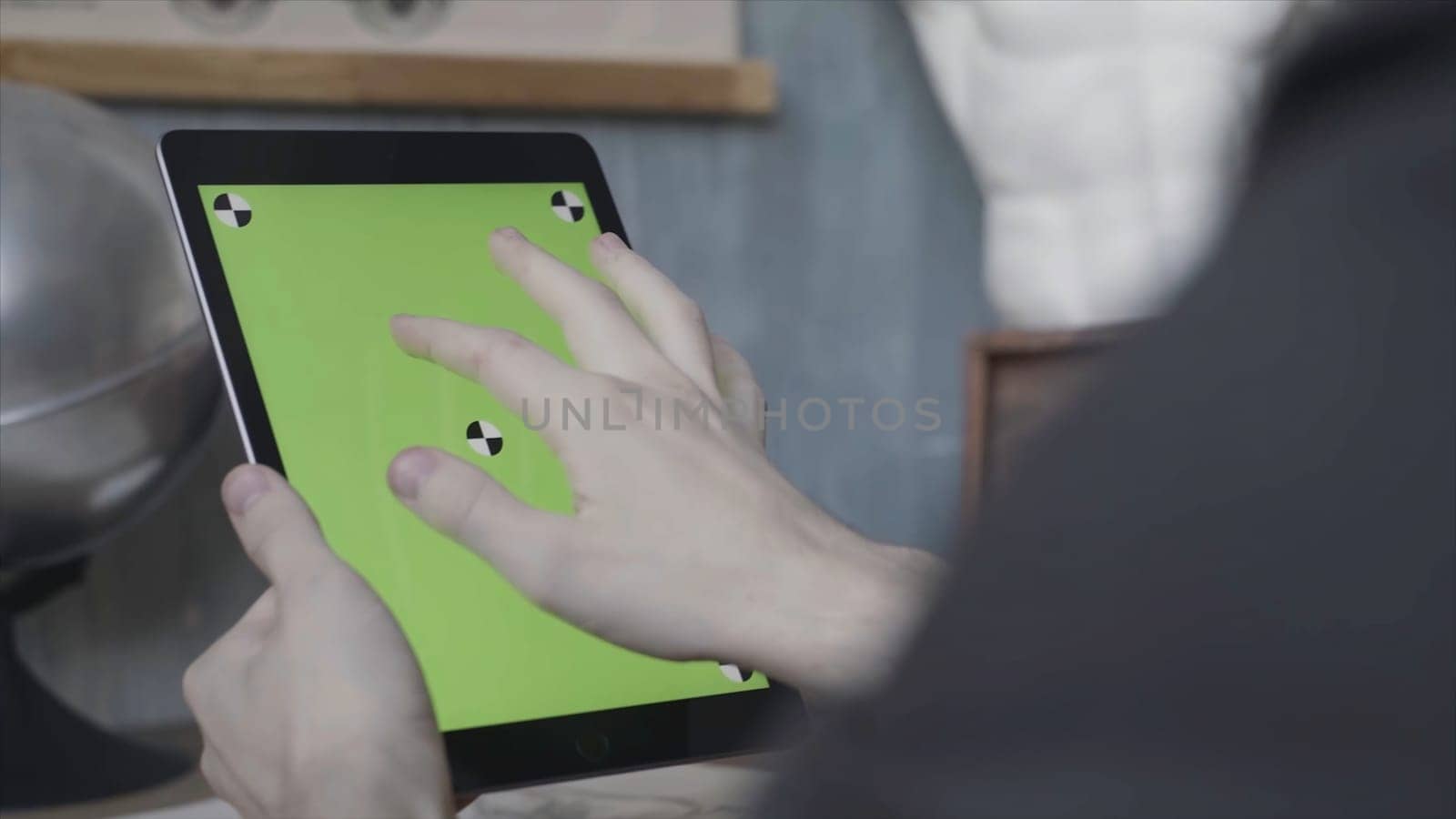 Hands of an unknown young guy tapping and scrolling on laptop with green screen on wooden table next to silver globe. Stock footage. Man using his Ipad with chroma key. by Mediawhalestock