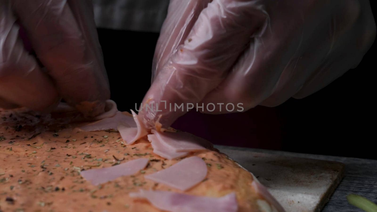 Cooking pizza slow motion. Frame. Making pizza with cheese, tomato paste, sausage and mustard. The work of the cook. The cook arranges pieces of sausage and pizza with cheese and tomato paste. Full process of sprinkle milled cheese, slice meat and warp dough. Vertical look.