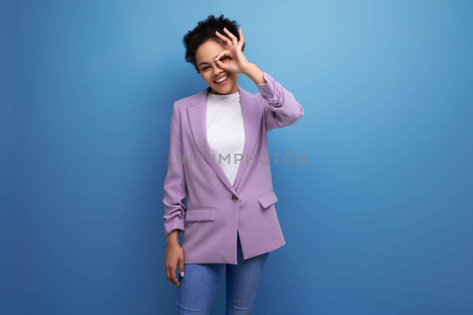 young charming successful hispanic business woman with curly hair dressed in a purple jacket on a blue background with copy space.