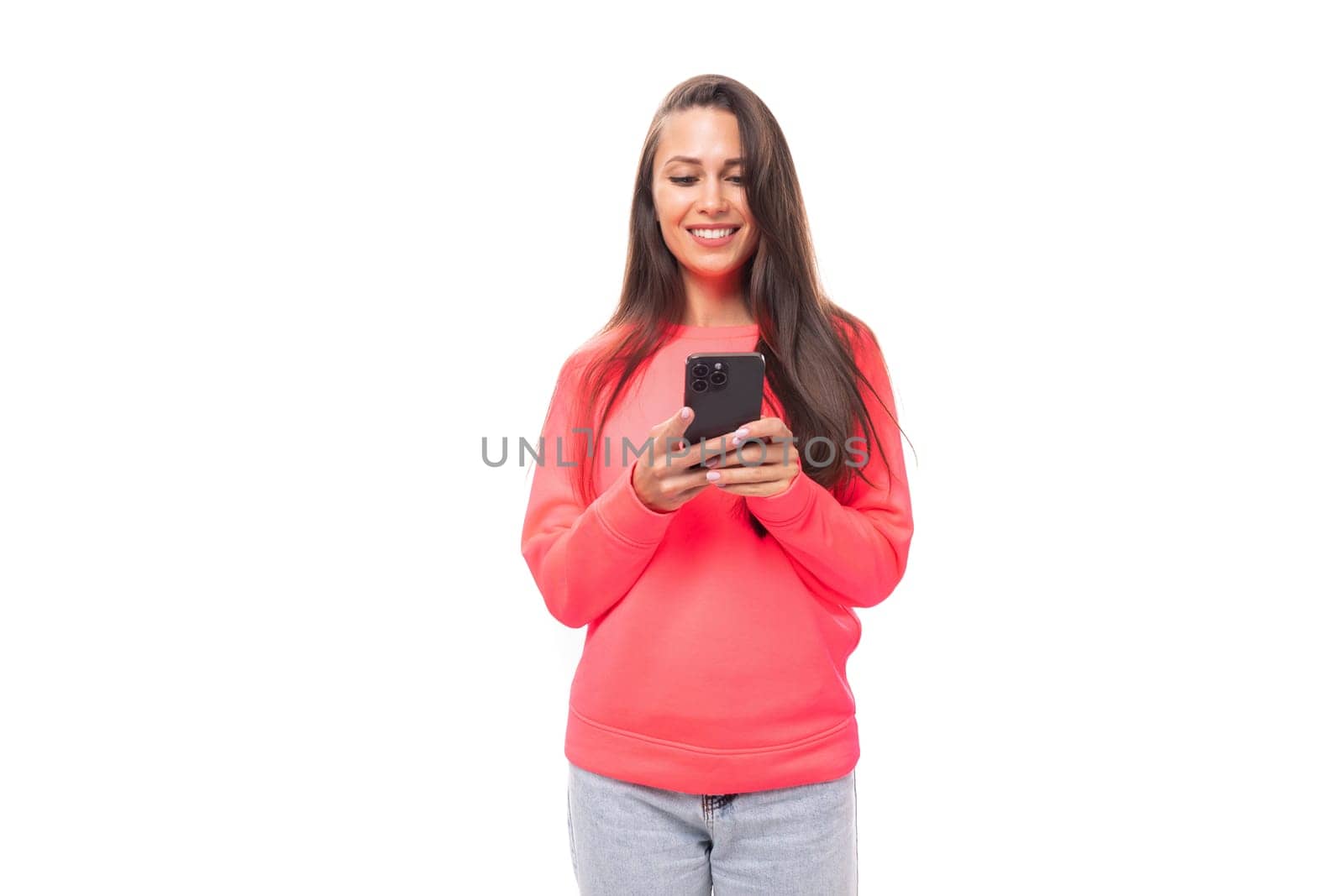 close-up of a young slender beautiful European lady with dark long straight hair in a pink sweater typing a message on a smartphone.