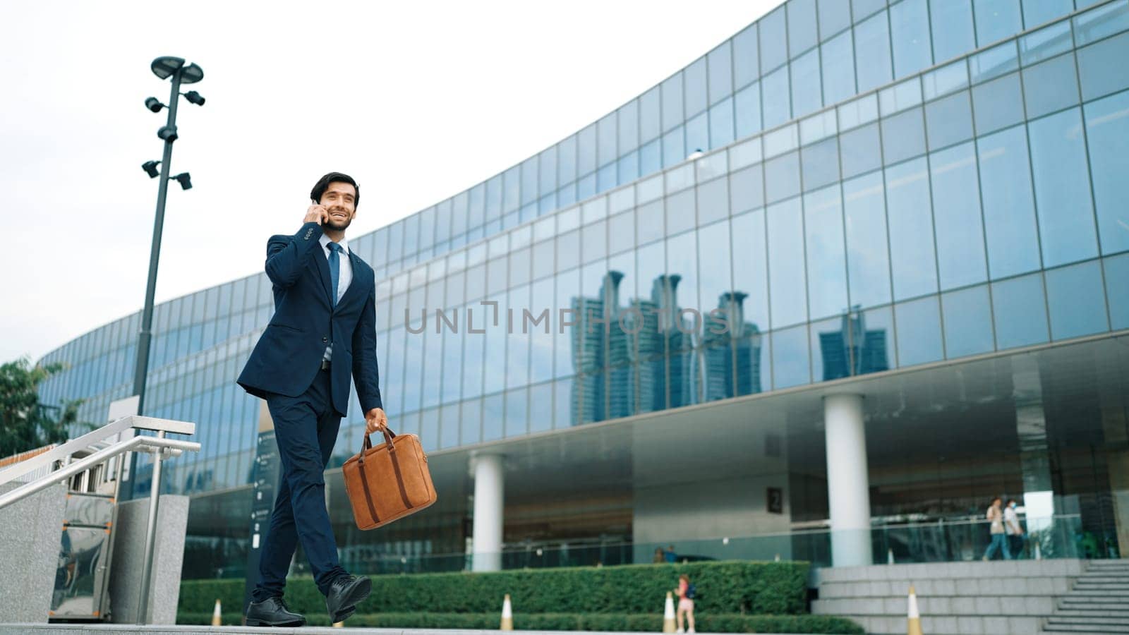Smart business man using phone to talking while walking at building. Happy manager walking at street while talking on smart phone to discuss business plan or marketing strategy or working. Exultant.
