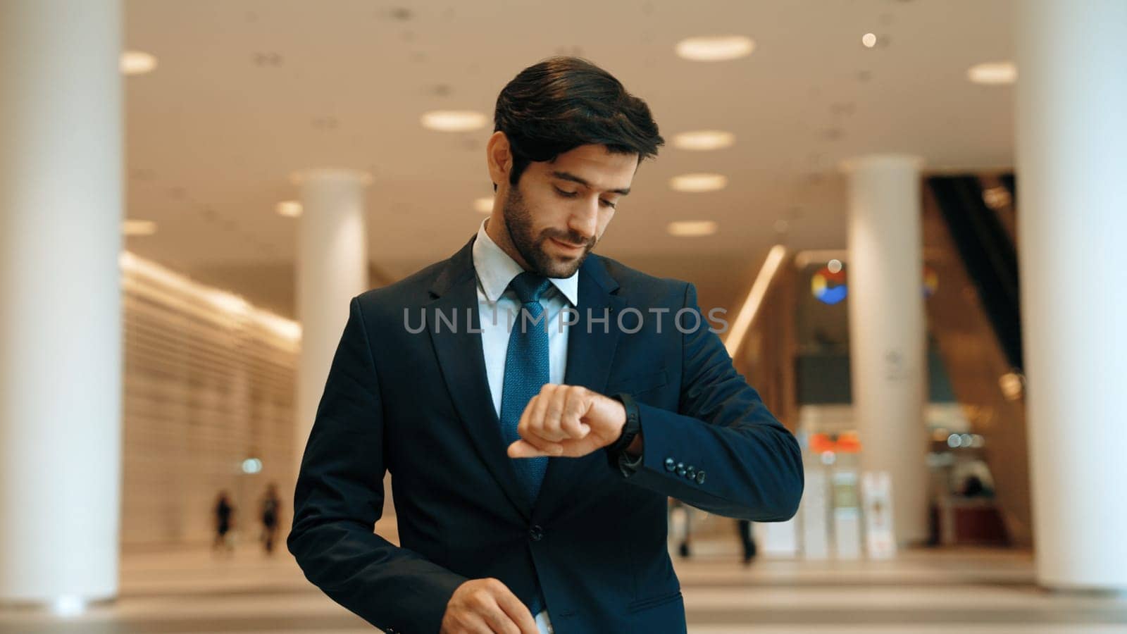 Caucasian smart business man looking at watch while waiting colleague. Executive manager wearing suit while standing at mall with blurred background. Investor wear blue suit check time. Exultant.