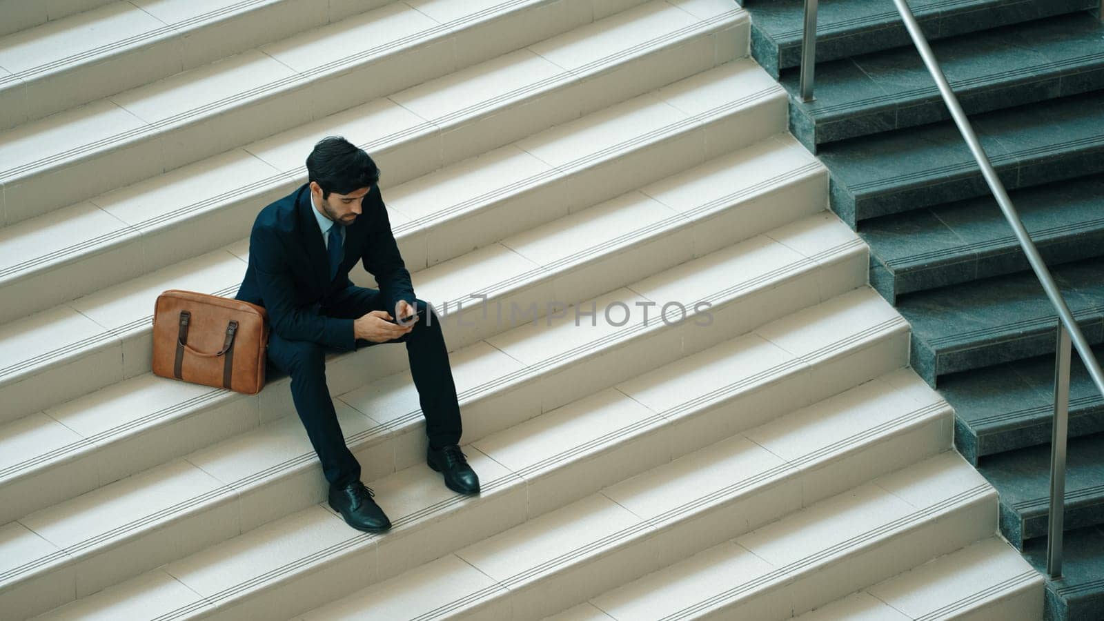 Business man sitting at stair while using mobile phone plan business strategy. Skilled project manager working by using smart phone contact business team or investor while wearing suit. Exultant.