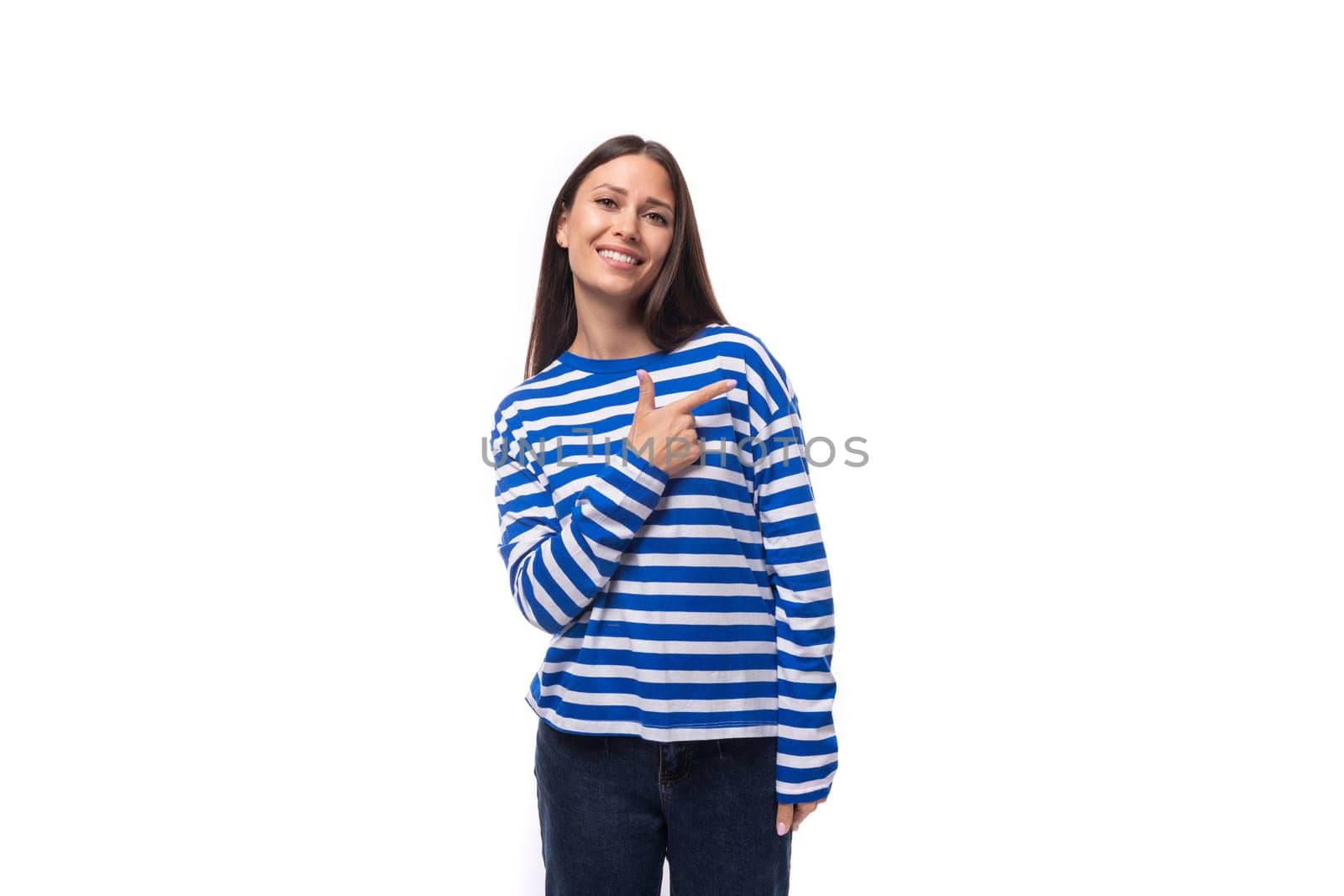 charming young brunette woman in a striped blue sweater points with her hand to the advertising space on a white background with copy space by TRMK