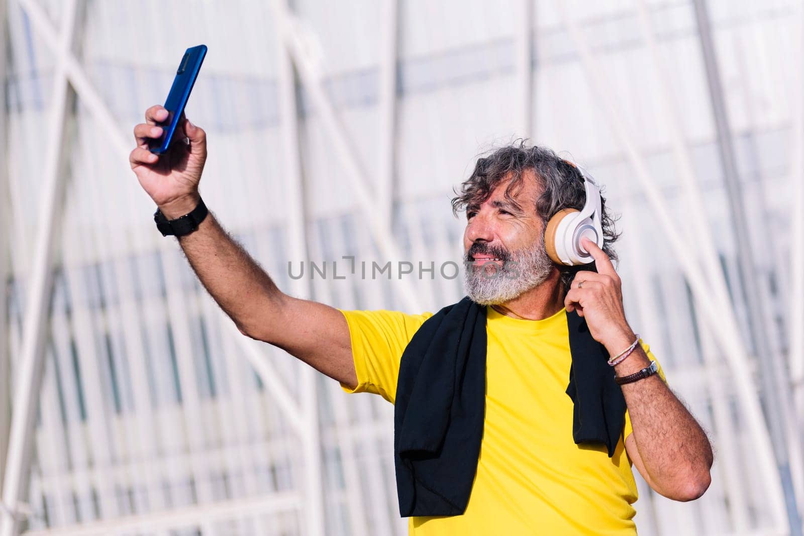 senior sports man listening to music with headphones while taking a selfie photo with his mobile phone, concept of active lifestyle in middle age