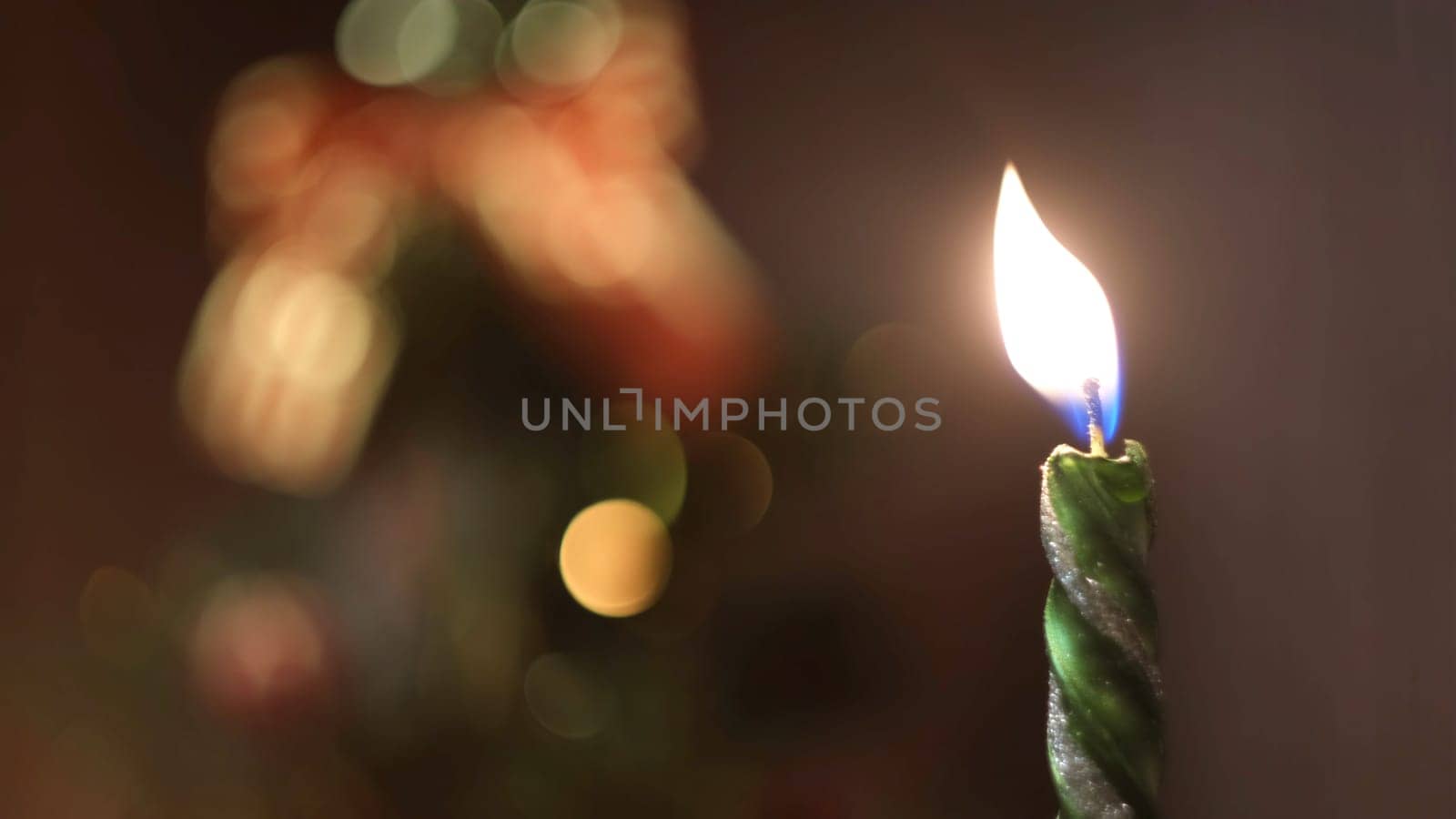 Close-up of lighted and extinction Christmas candle against the blurred Christmas tree silhouette with lights and decorations. Christmas mood