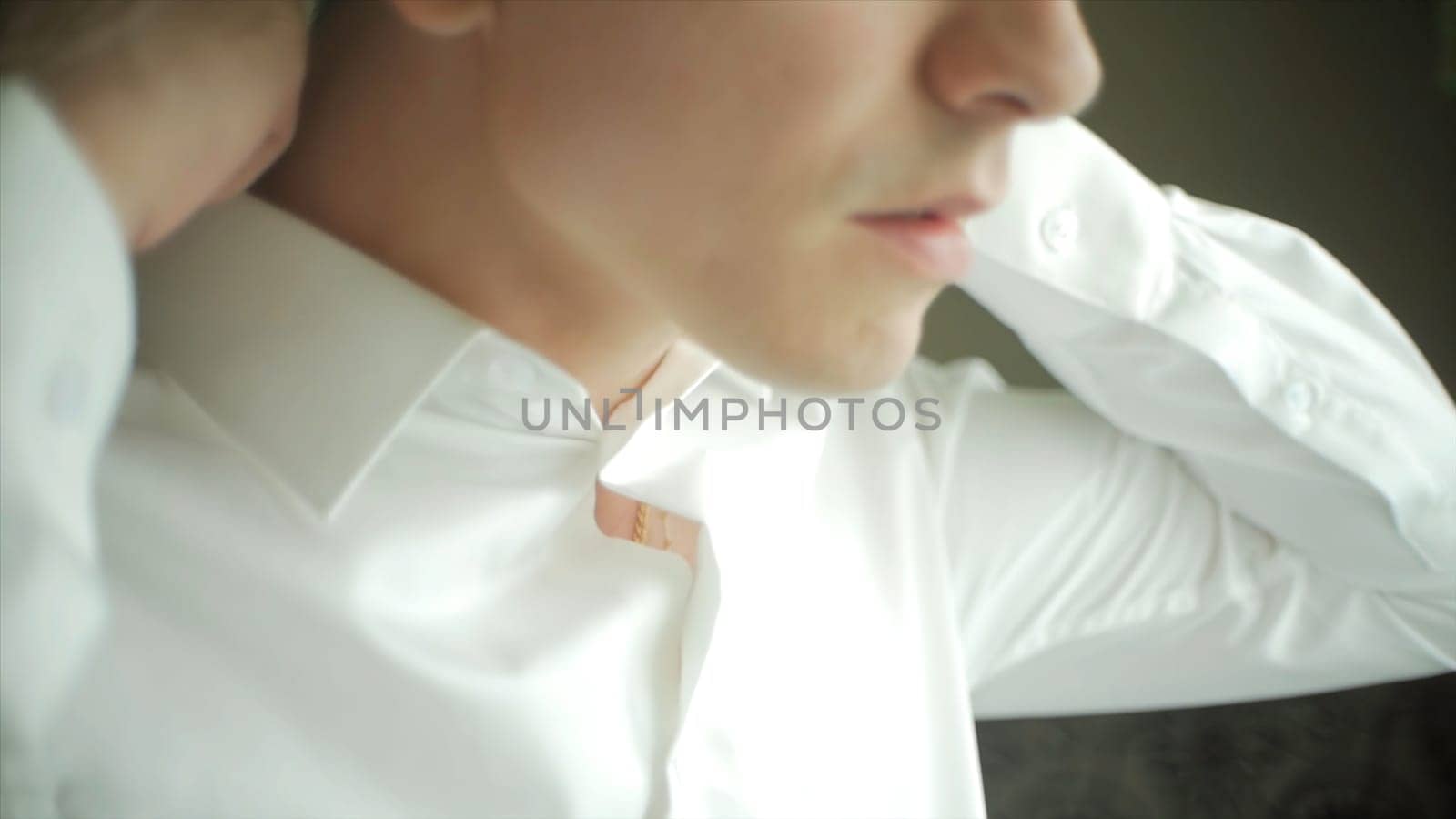 Man buttons up his white shirt standing in the front of a bright window. Clip. People, business, fashion and clothing concept - close up of man dressing up and fastening buttons on shirt at home.