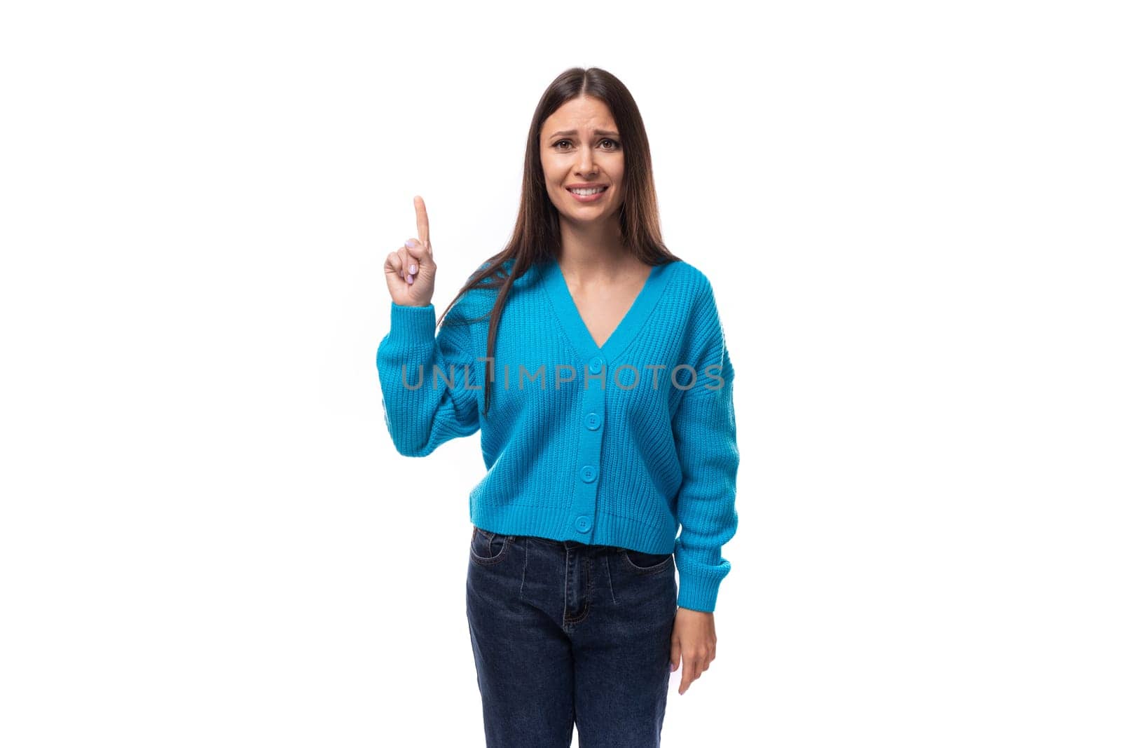 young pretty european brunette woman dressed in a blue cardigan points her fingers at the advertising space.
