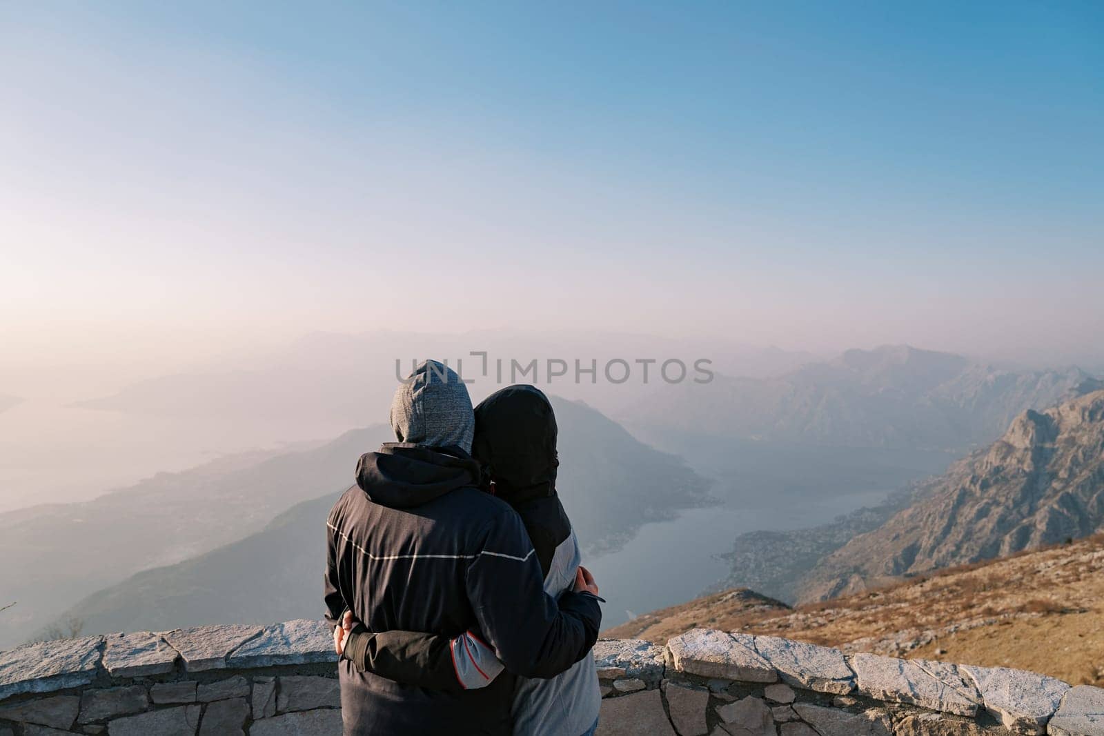 Man and woman are hugging on a mountain looking at the Bay of Kotor in the fog. Montenegro. Back view. High quality photo