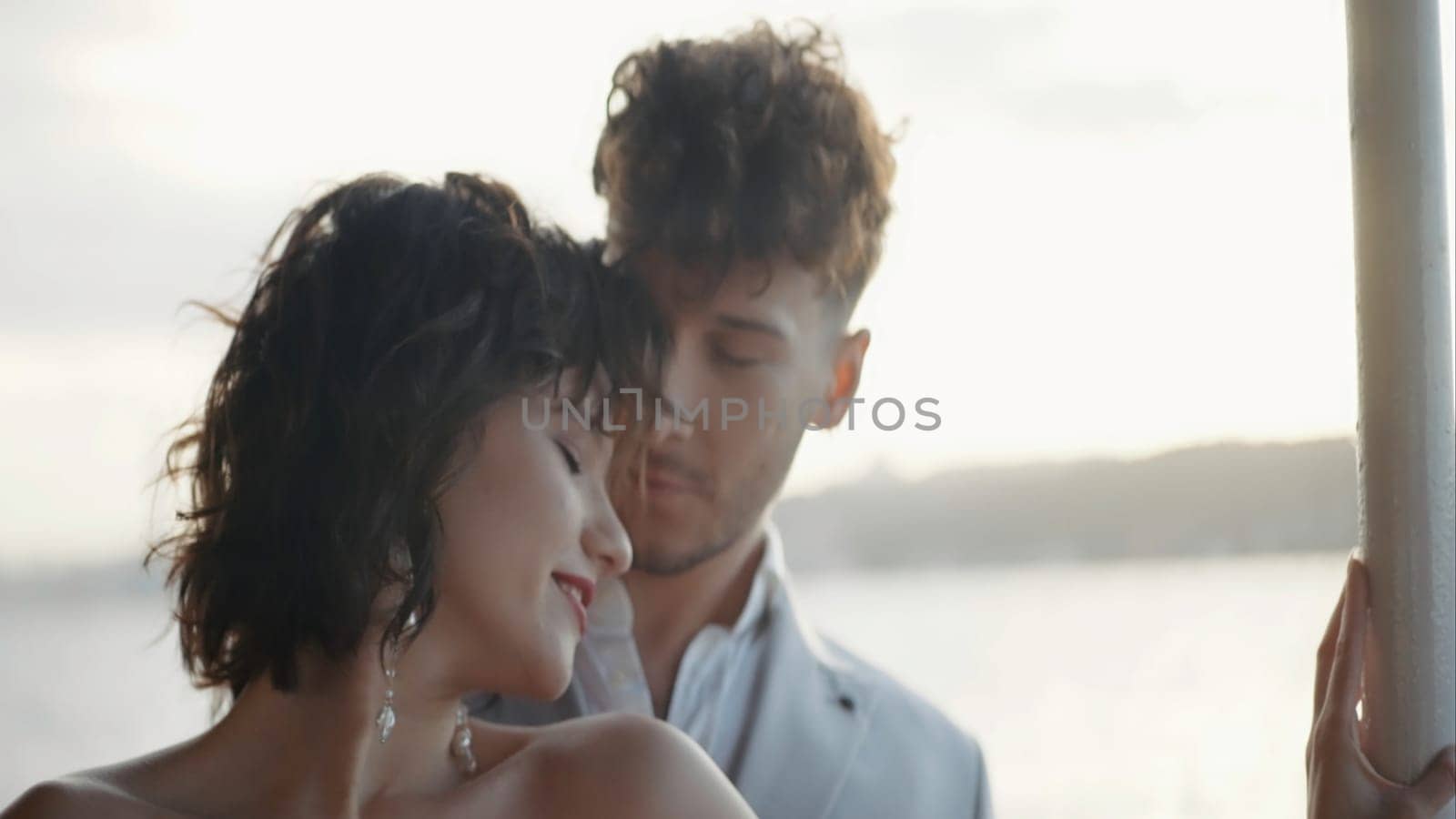 Handsome man and beautiful woman on a date near the river embracing and laughing. Action. Female with curly short hair and a loving guy behind her outdoors
