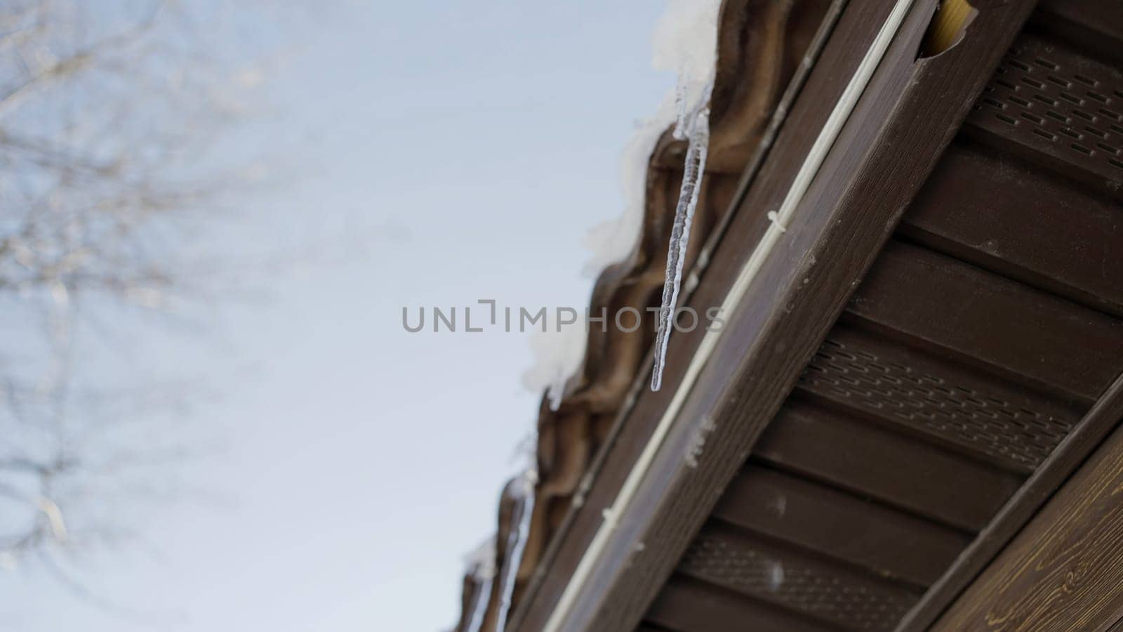 Winter roof. Action.A landscape where you can see large icicles dripping down hanging on top of the house and you can see the blue sky. High quality 4k footage