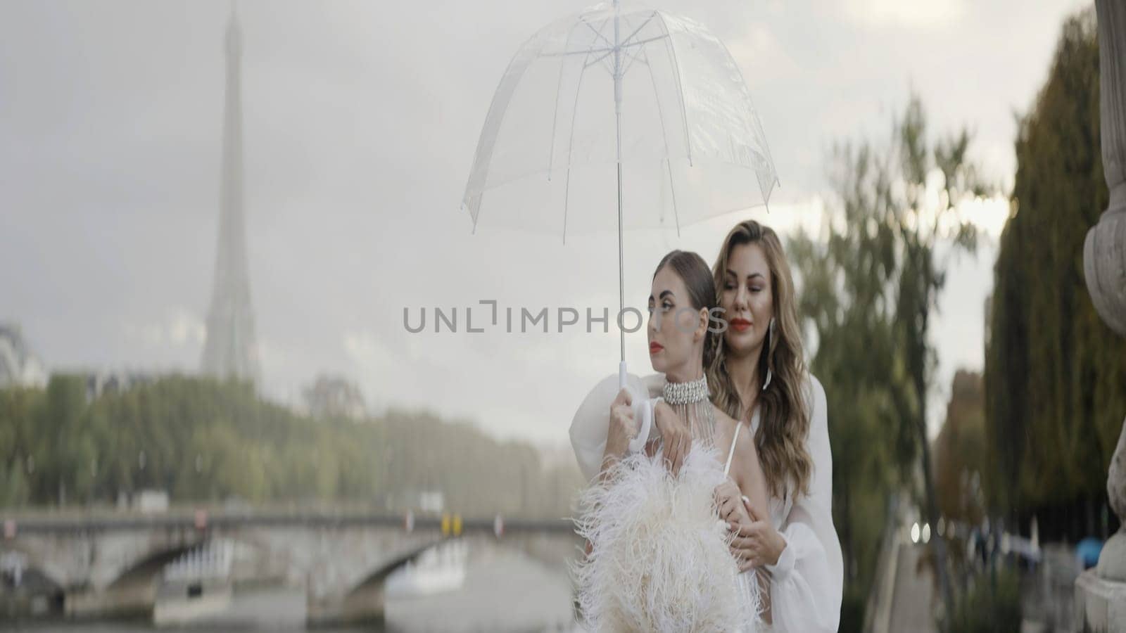 Two bright female models portrait. Action. Stunning women with red lips with a transparent umbrella and the Effel Tower on the background