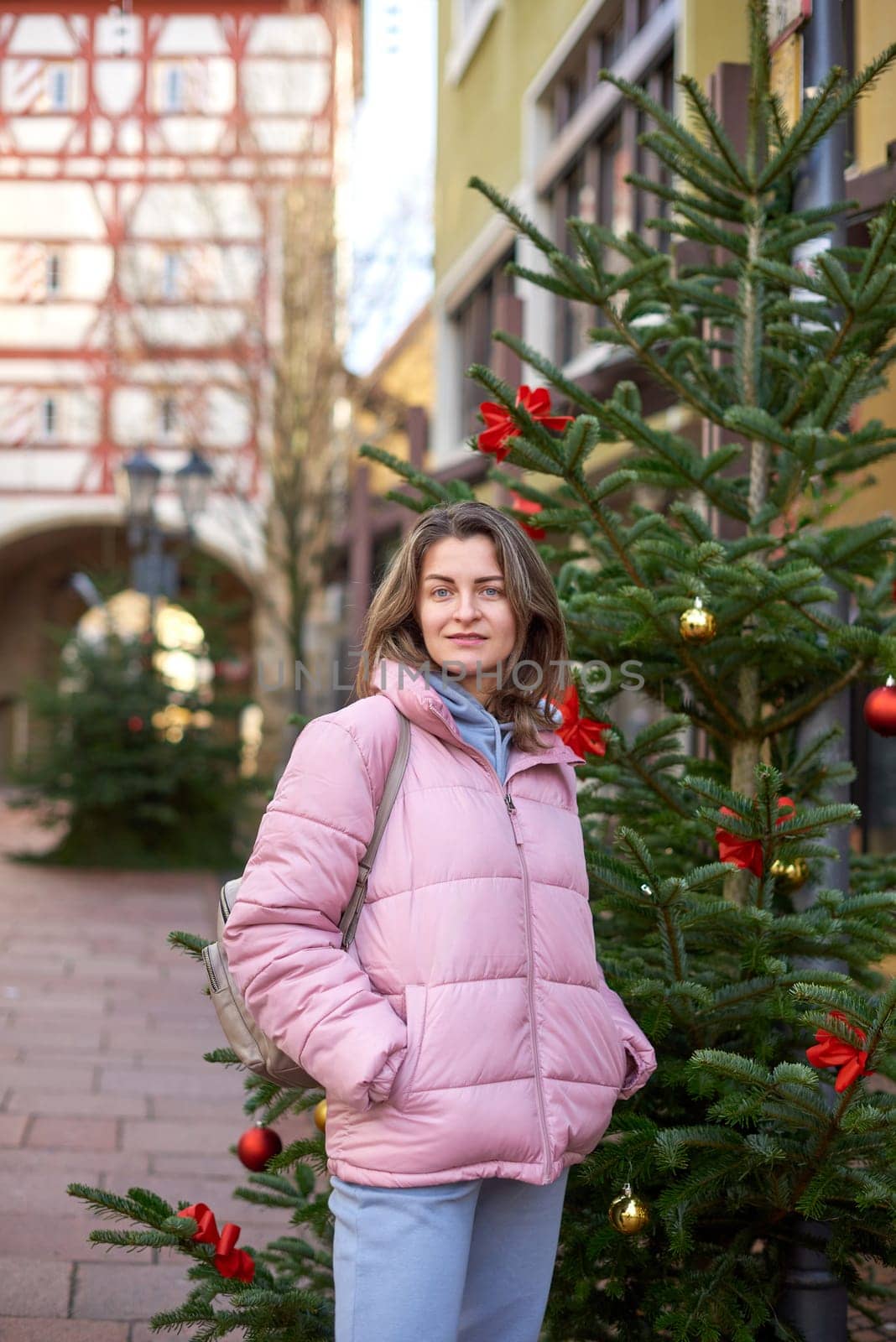 A beautiful girl stands on the street of the old European town of Bietigheim-Bissingen in Germany on Christmas Eve. City streets are decorated with Christmas trees and New Year's decorations, tourism, fashion, historical places, Europe by Andrii_Ko