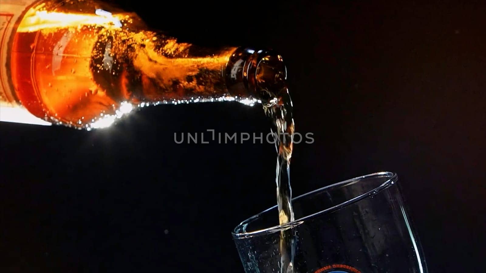 Close up of pouring beer from the glass brown bottle into the glass. Video. Pouring alcoholic drink isolated on black background, concept of party