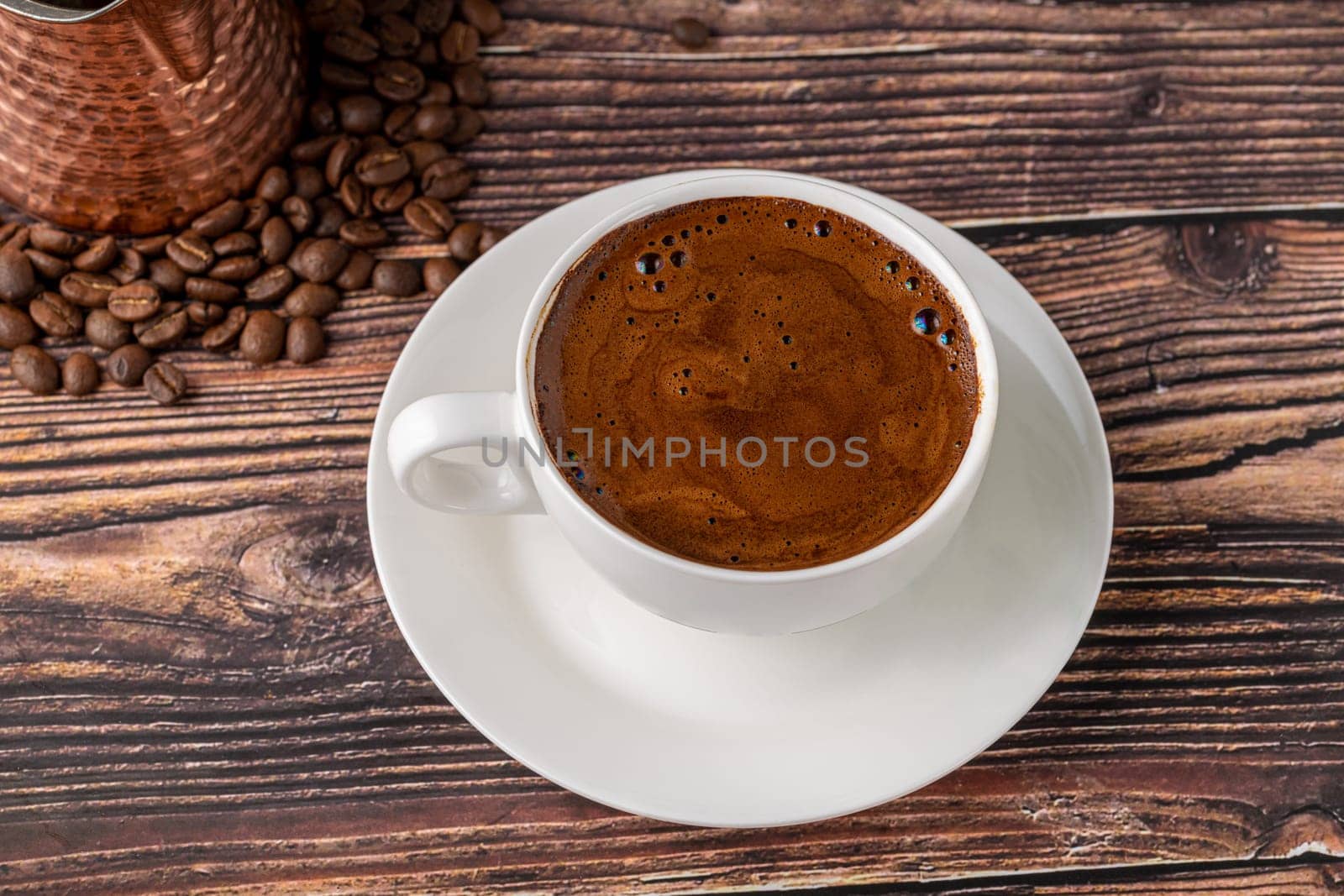 Double Turkish coffee in a white porcelain cup with a decorative coffee pot on a wooden table