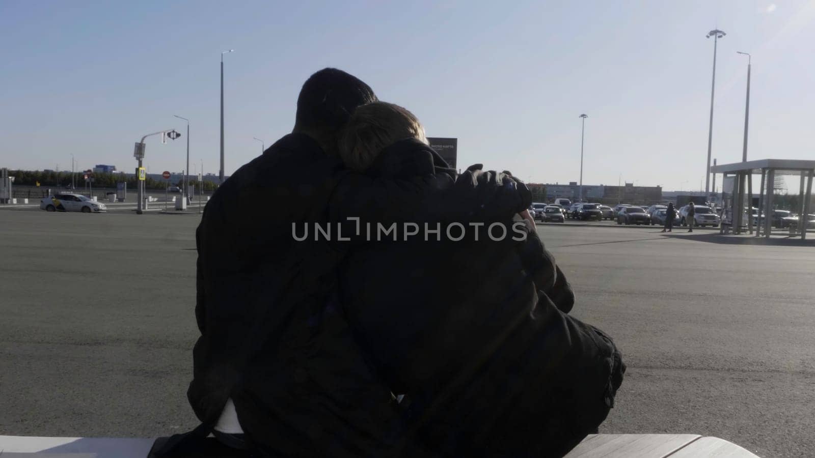 Young gay male couple sitting on a bench at bus stop, talking, and hugging. HDR. Two men in love waiting for a bus outdoors during conversation on a sunny day, concept of lgbt relationships